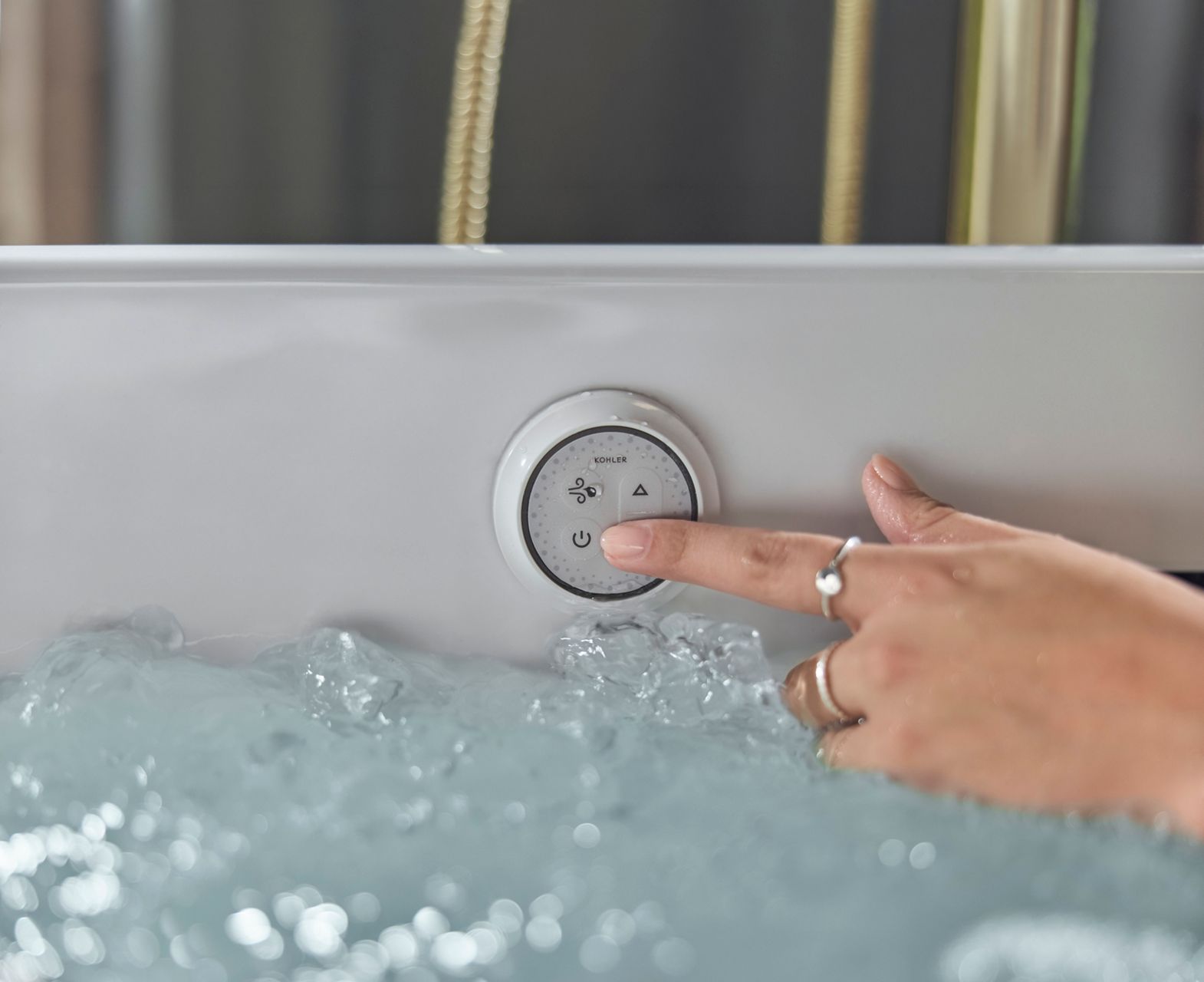 Close-up of a hand pressing the integrated bathtub control while the tub is filled with bubbling water, highlighting the hydrotherapy controls.