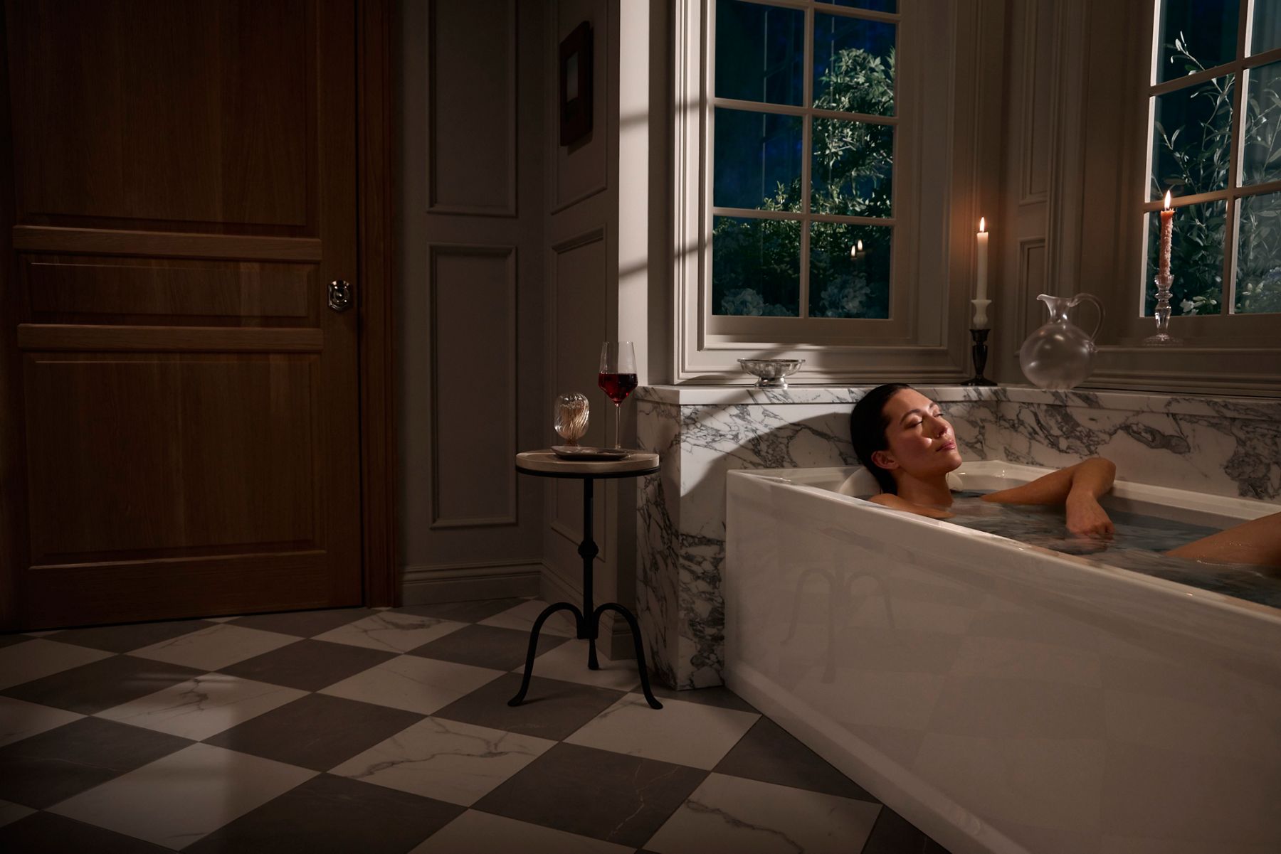 Luxury bathroom featuring a person relaxing in a rectangular bathtub with a marble surround, large windows, and candlelit accents creating a serene spa-like setting.