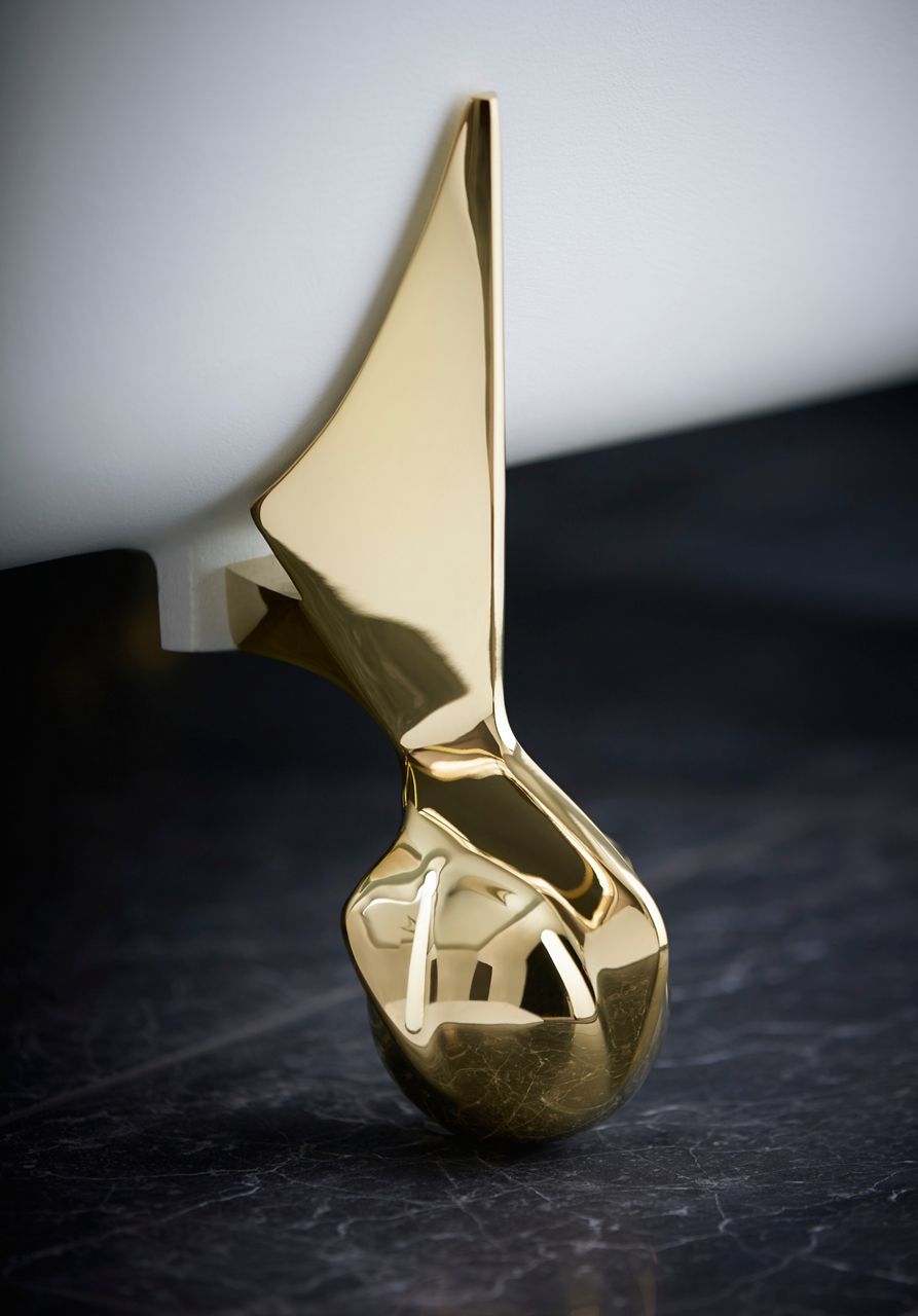 Close-up of a polished gold bathtub overflow cover, highlighting its sculptural design and premium finish.