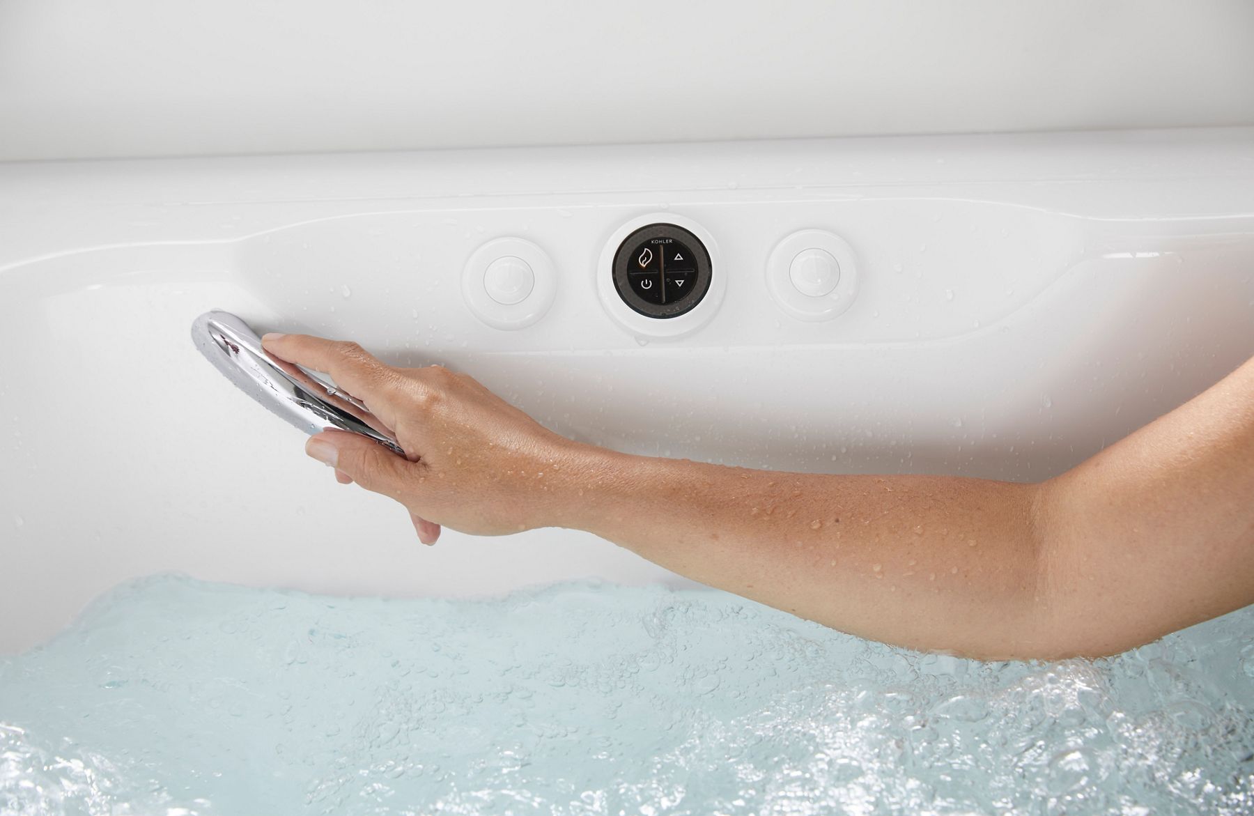 Close-up of a hand holding the bathtub handshower above bubbling water, highlighting the integrated controls and hydrotherapy bathing experience.