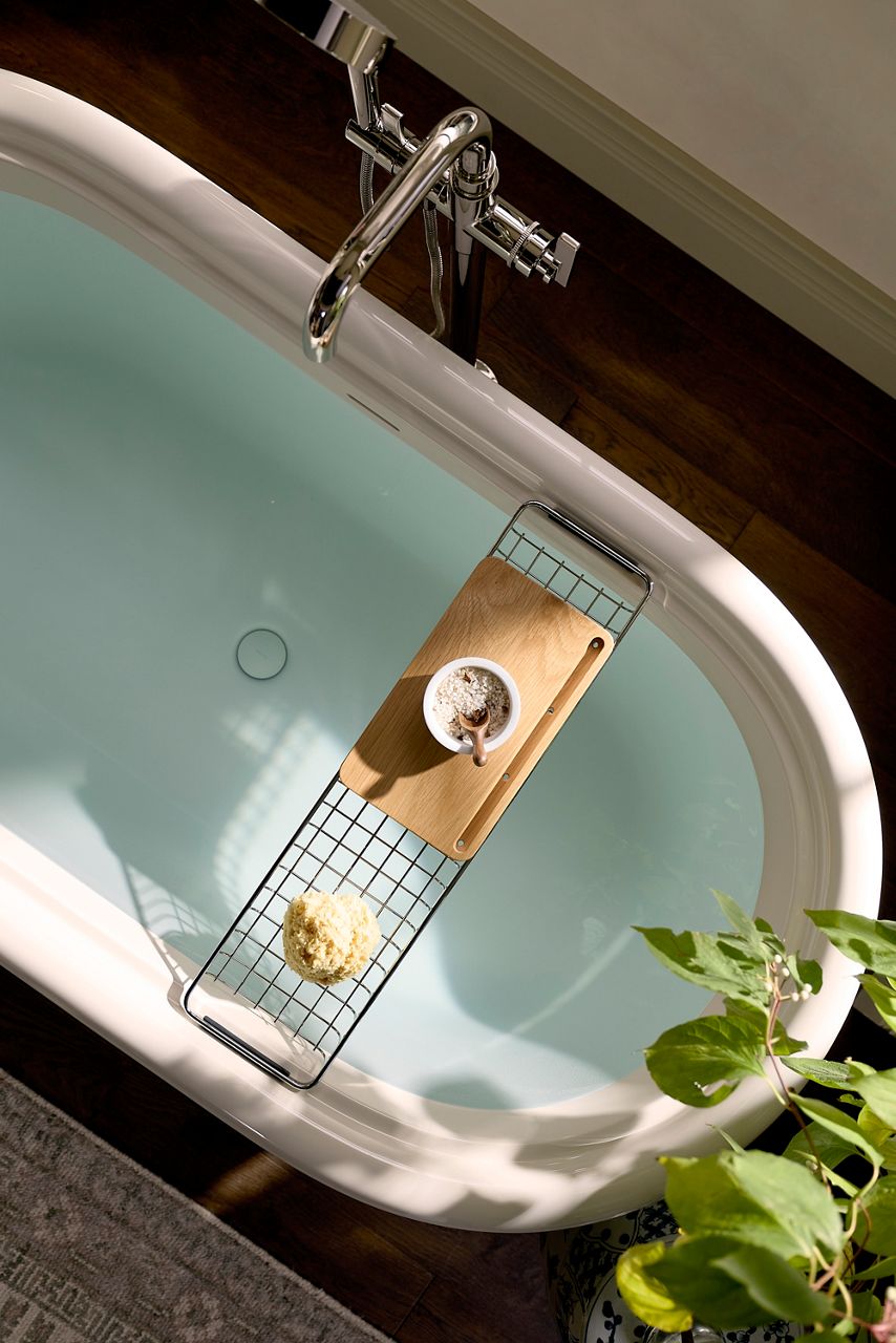 Overhead view of a freestanding bathtub featuring the Claude™ by Studio McGee two-piece bath caddy, chrome faucet, and patterned wallpaper in the Shea McGee x Kohler Claude primary bathroom.