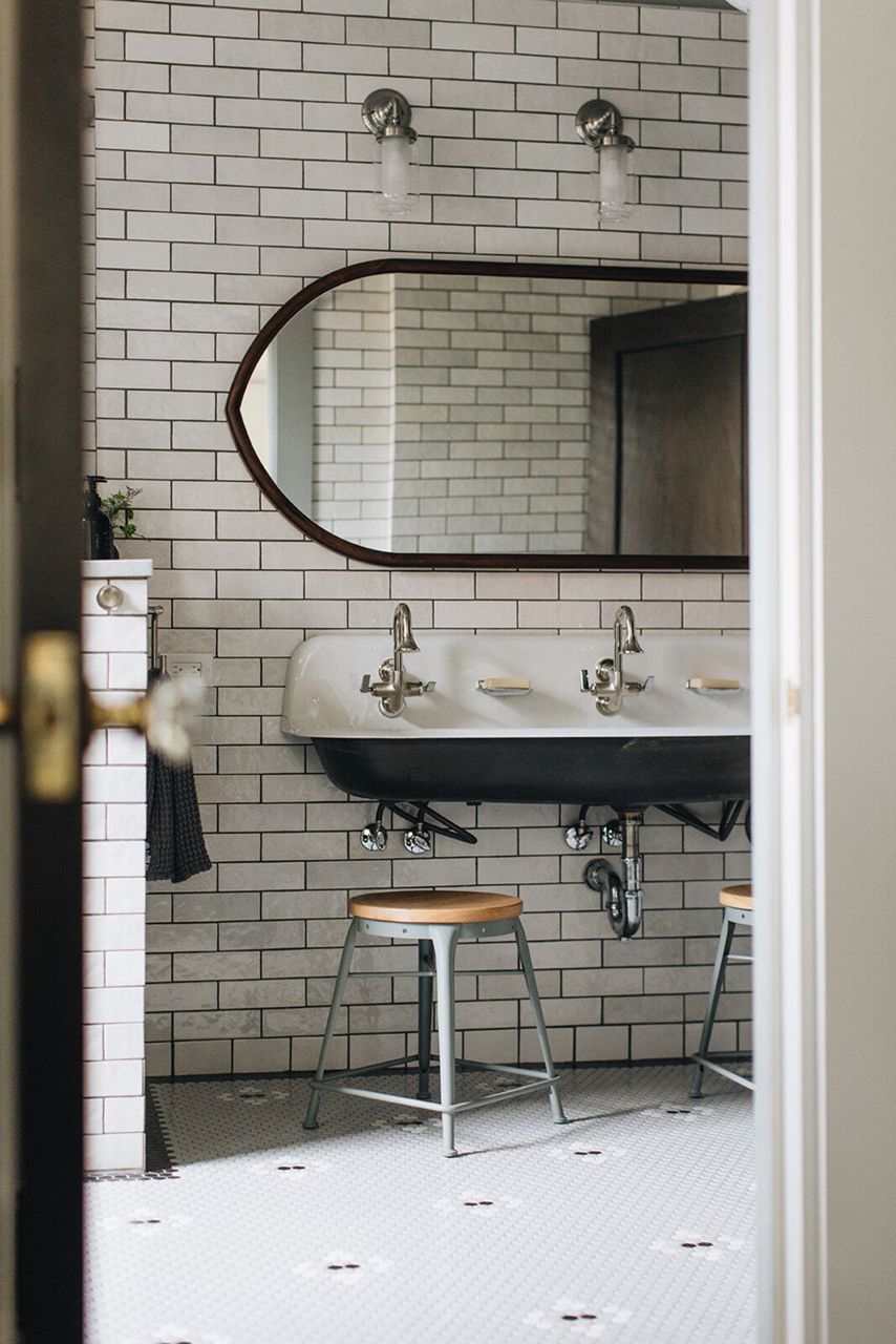 Salle de bain en noir et blanc, avec un grand lavabo mural en fonte émaillée, un carrelage de style métro et des touches argentées.