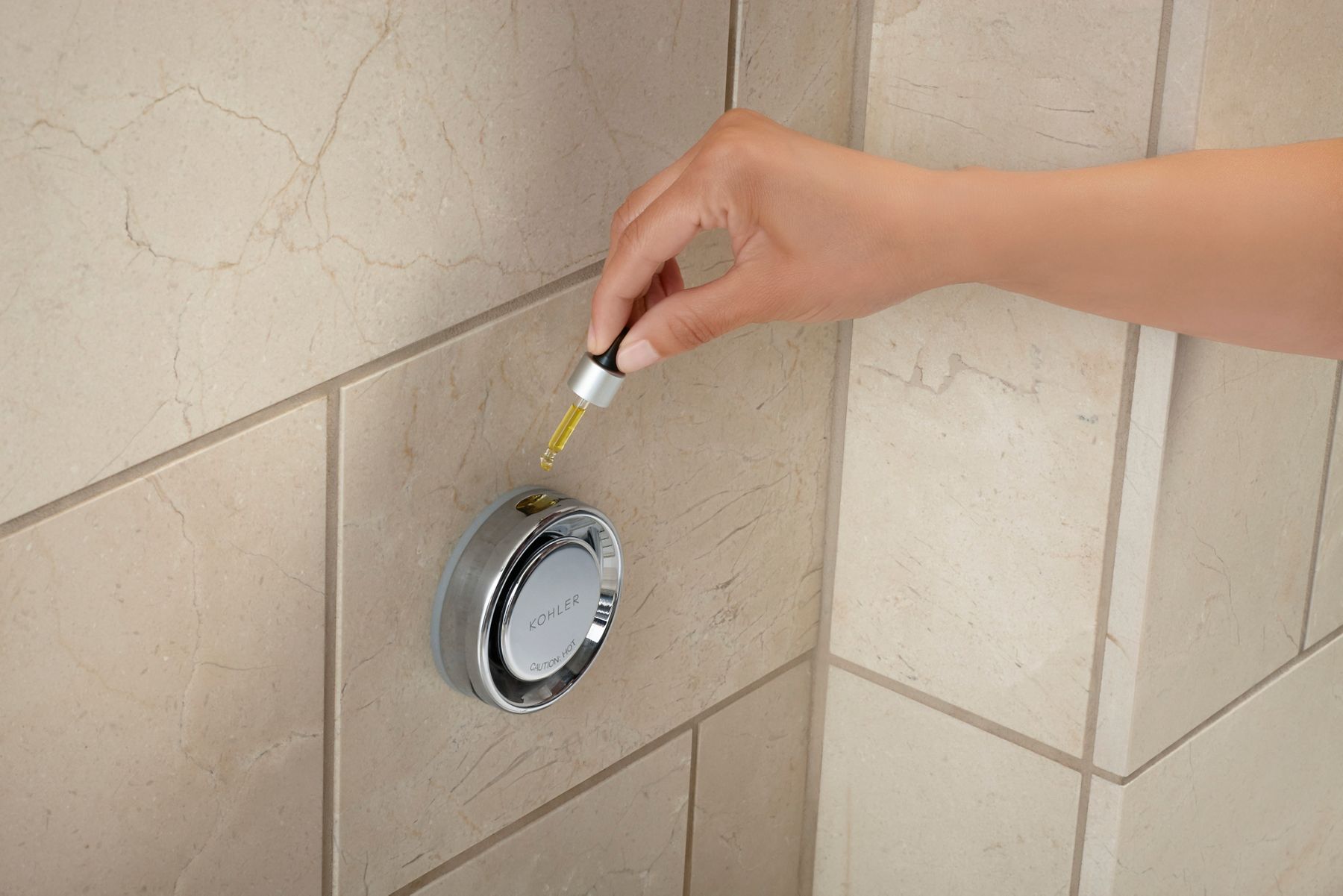 Close-up image of a person's hand dripping essential oils into the KOHLER steam shower product to infuse the steam with natural oils. 
