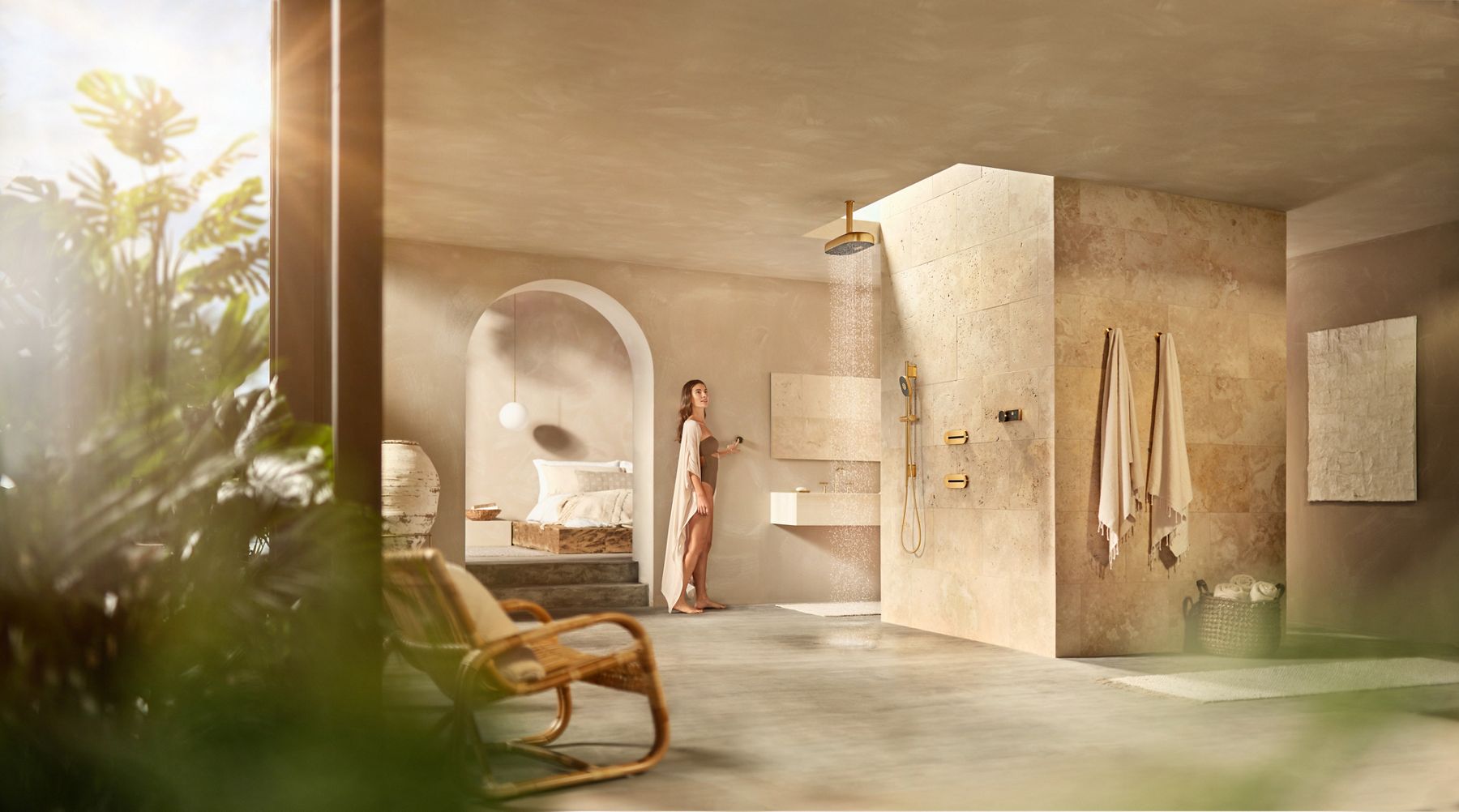 A woman in a large bathroom with stone tile from floor to ceiling stands at a distance while she turns on the statement rain showerhead.
