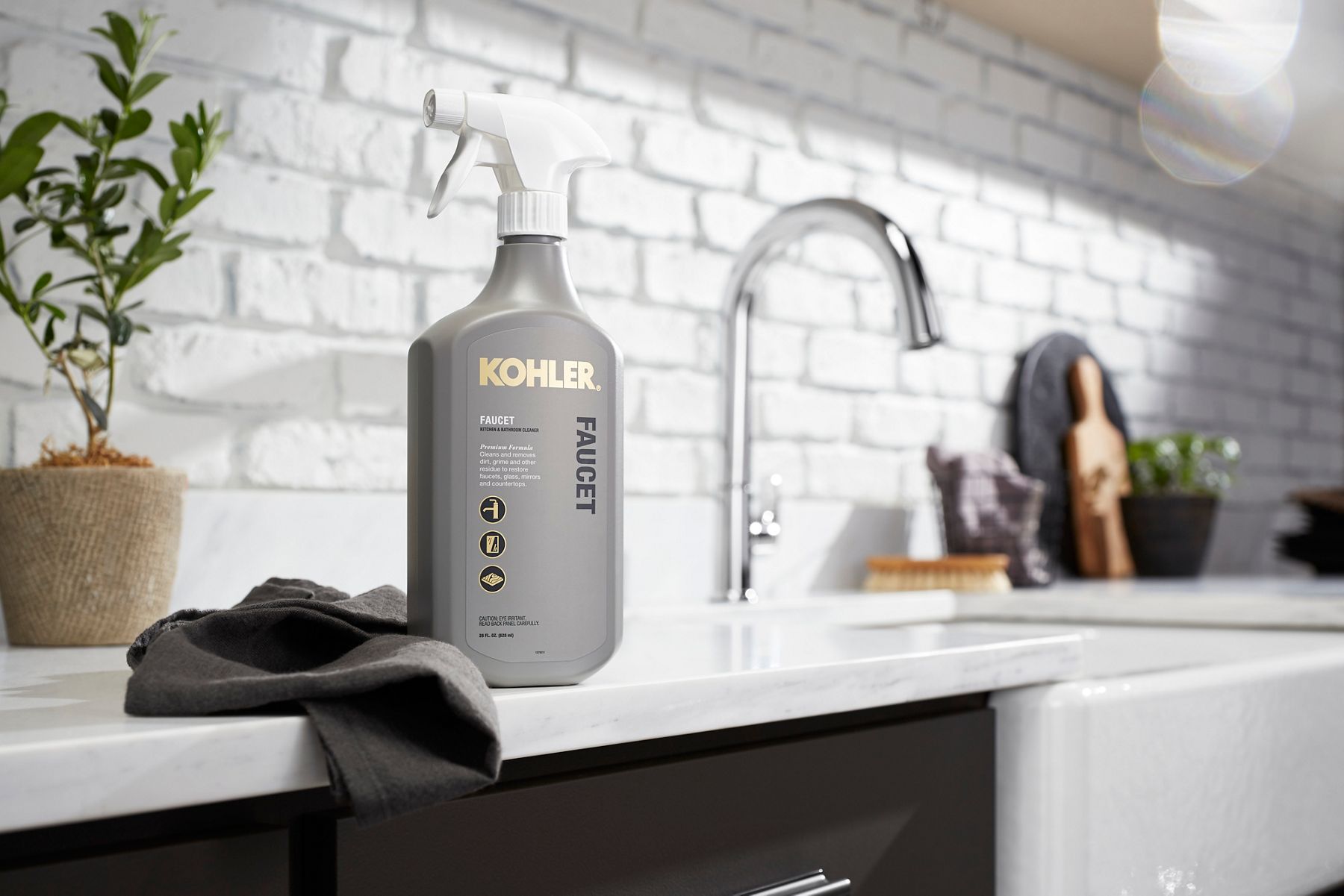 A man uses a cloth and Kohler Faucet Cleaner to clean a mirror in a bathroom with white counters, round bowl sink, and polished chrome single handle faucet.