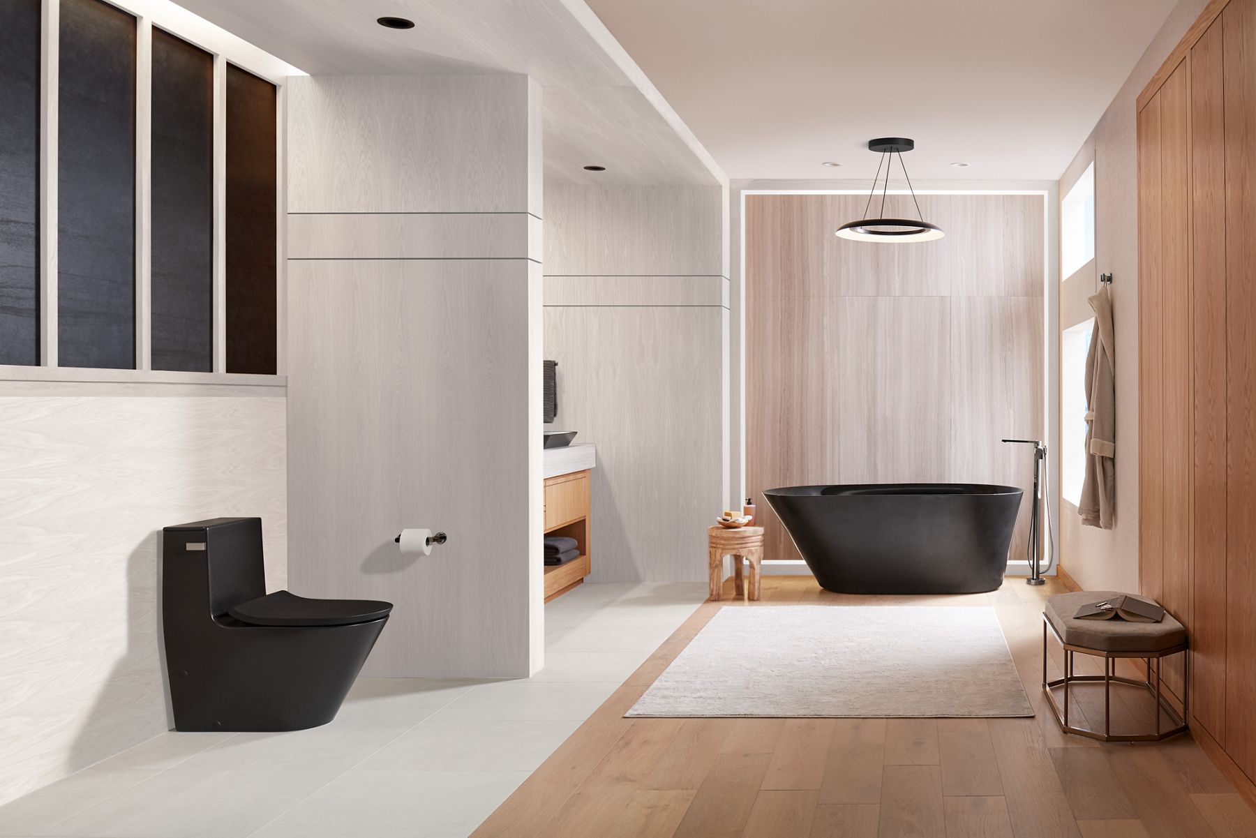A modern minimalist bathroom in a range of neutral tones with a black one-piece toilet in the left foreground and a vanity to its side.