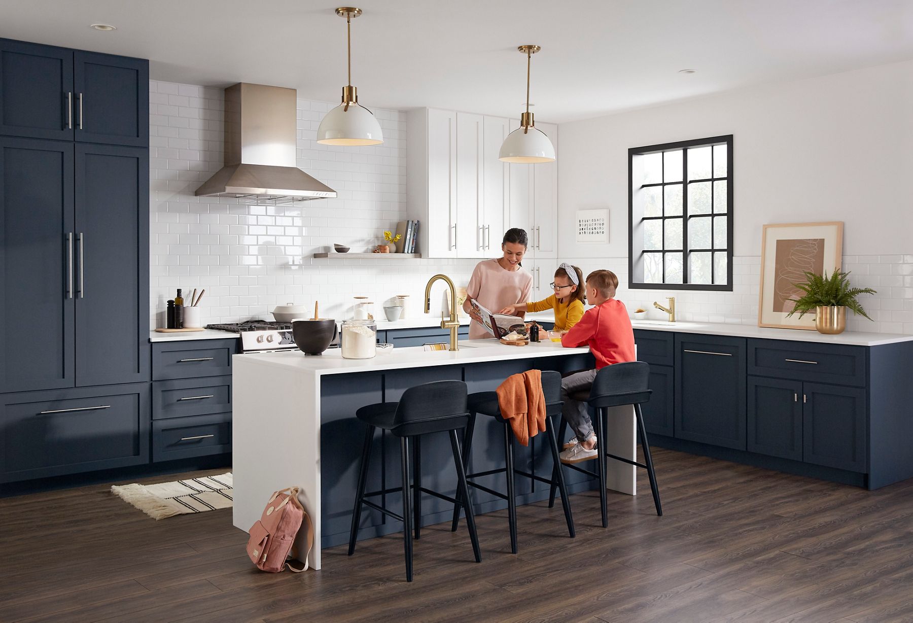 Une famille dans une cuisine moderne avec des armoires bleu marine et blanches, des accents dorés et un grand îlot avec places assises, qui passe du bon temps ensemble.