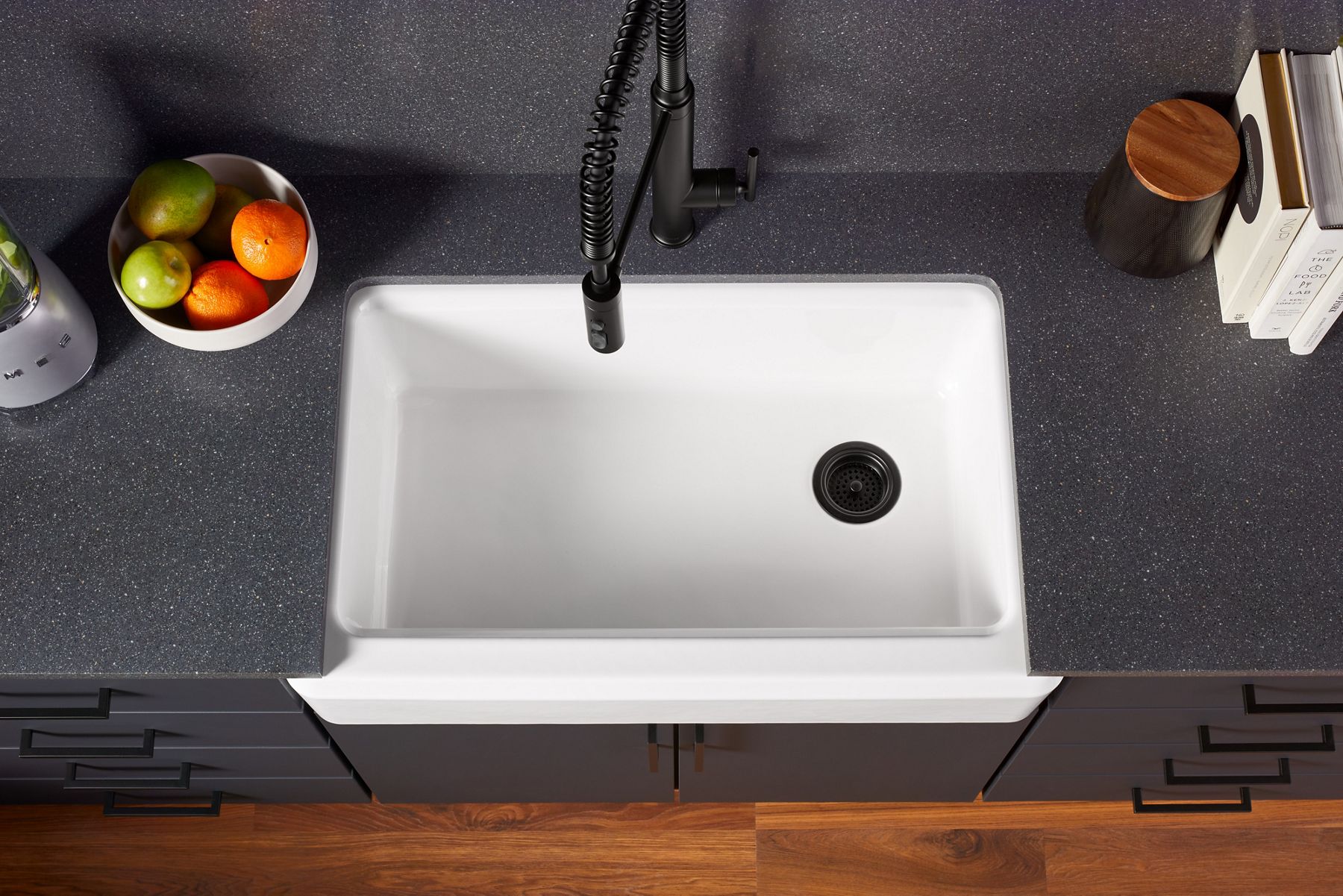 Overhead view of a white apron front single-bowl sink set in a dark indigo counter top with a matte black semiprofessional faucet.