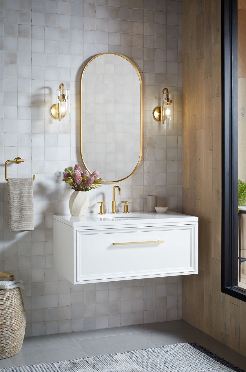 A KOHLER Purist widespread lavatory faucet with gooseneck and cross handles installed on a white vanity top underneath a capsule mirror.