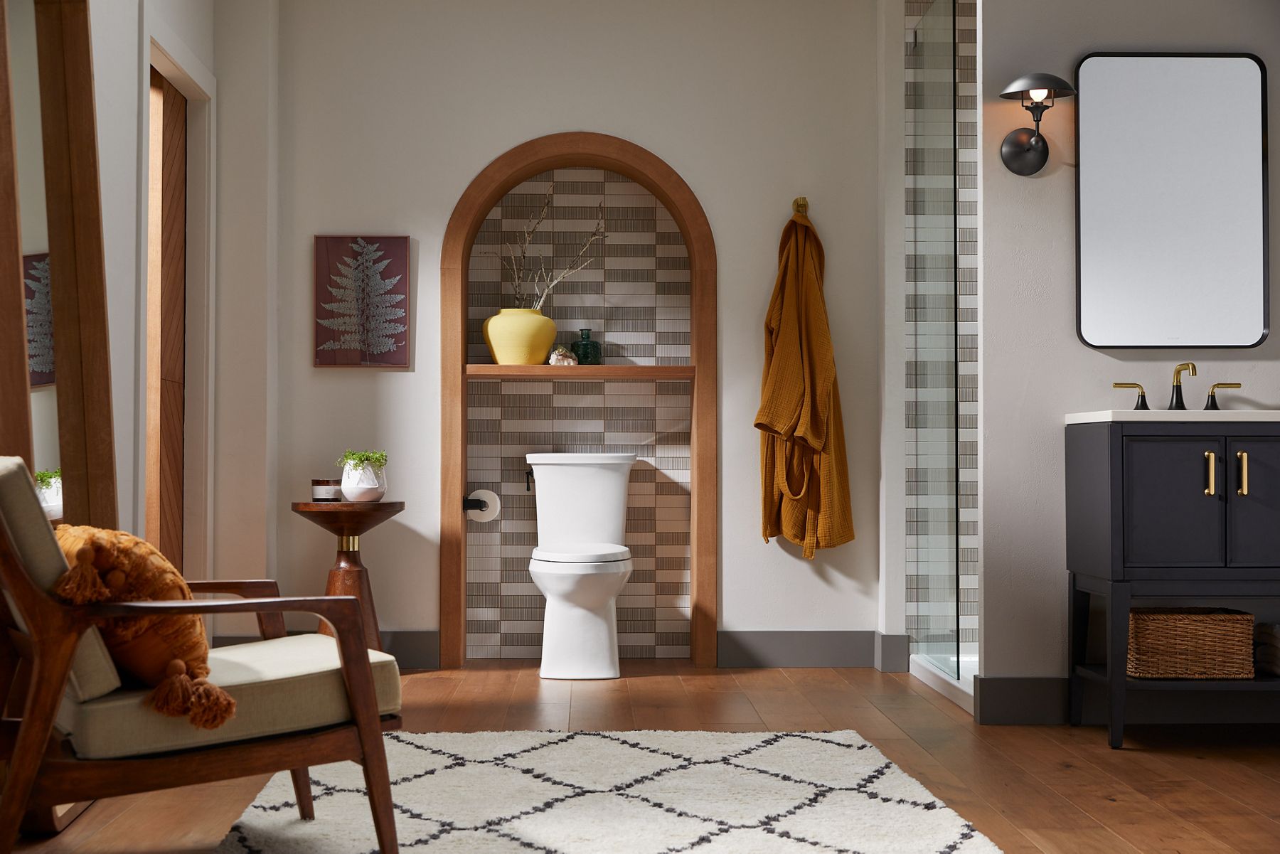 A two-piece WaterSense-labeled toilet in front of a tile wall with two different neutral colors set in a random pattern.