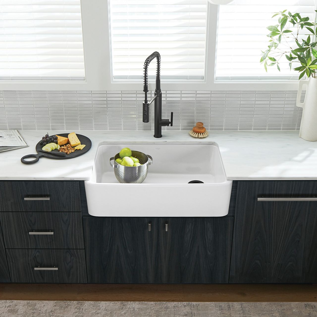 A KOHLER enameled cast iron kitchen sink with an apron front and a matte black faucet.