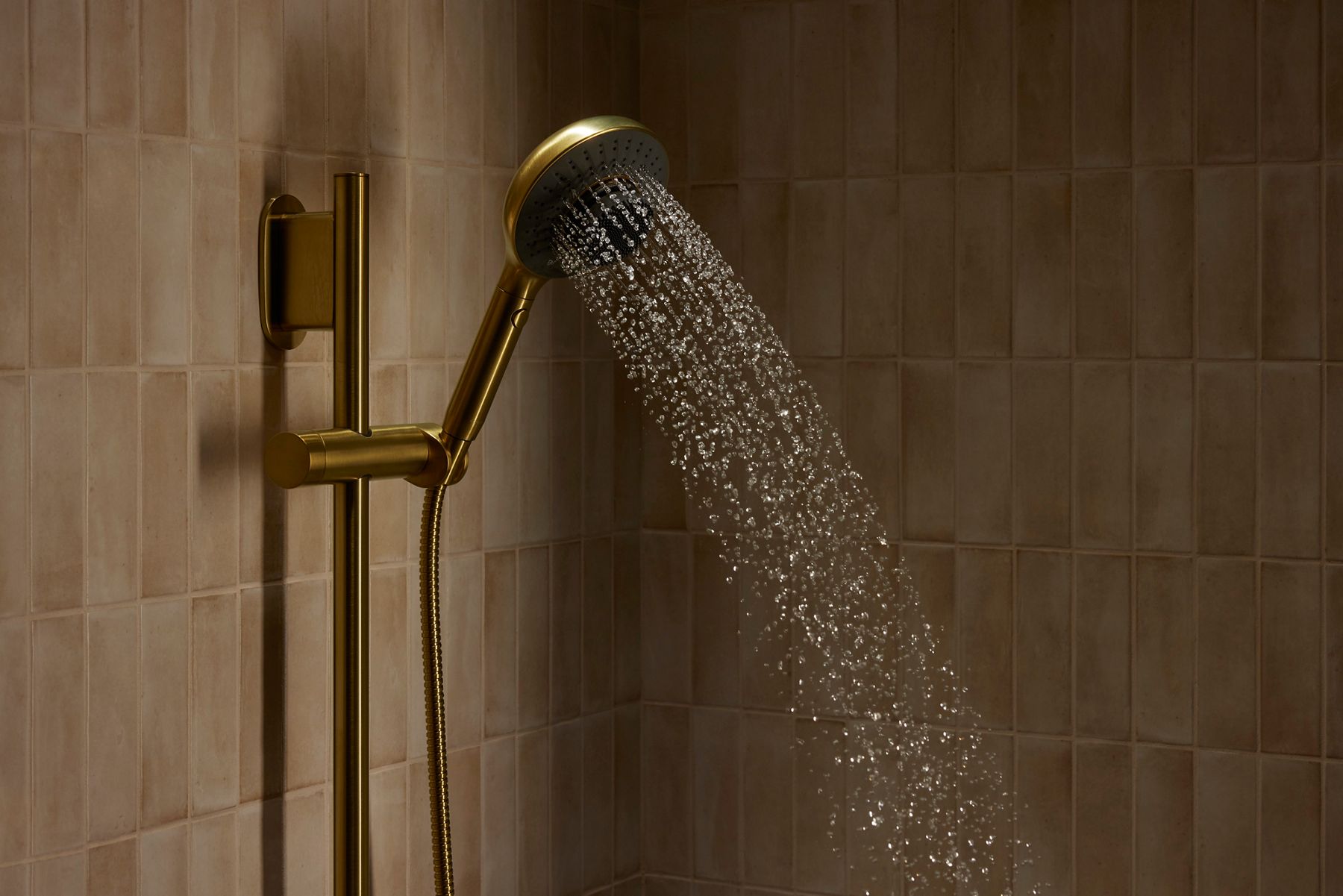 Gold handshower mounted on a wall spraying a focused stream of water.