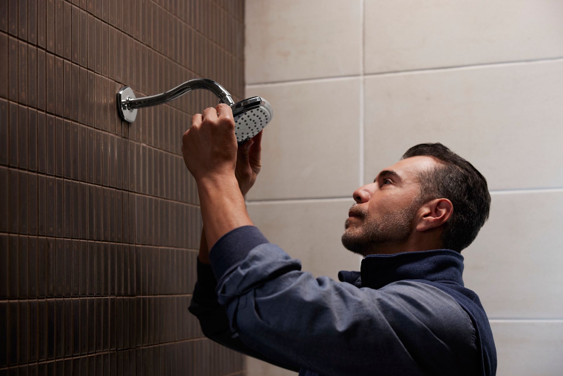 Une personne debout dans une douche installant une nouvelle pomme de douche sur le bras de douche.