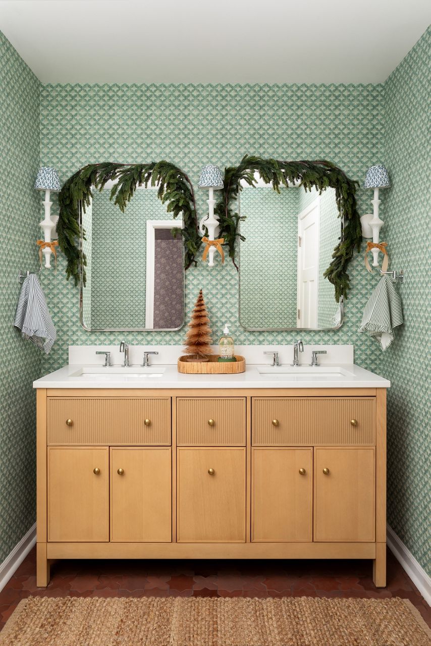 Chasing Paper’s bathroom with light wood vanity, double mirrors, and festive greenery around the sink.