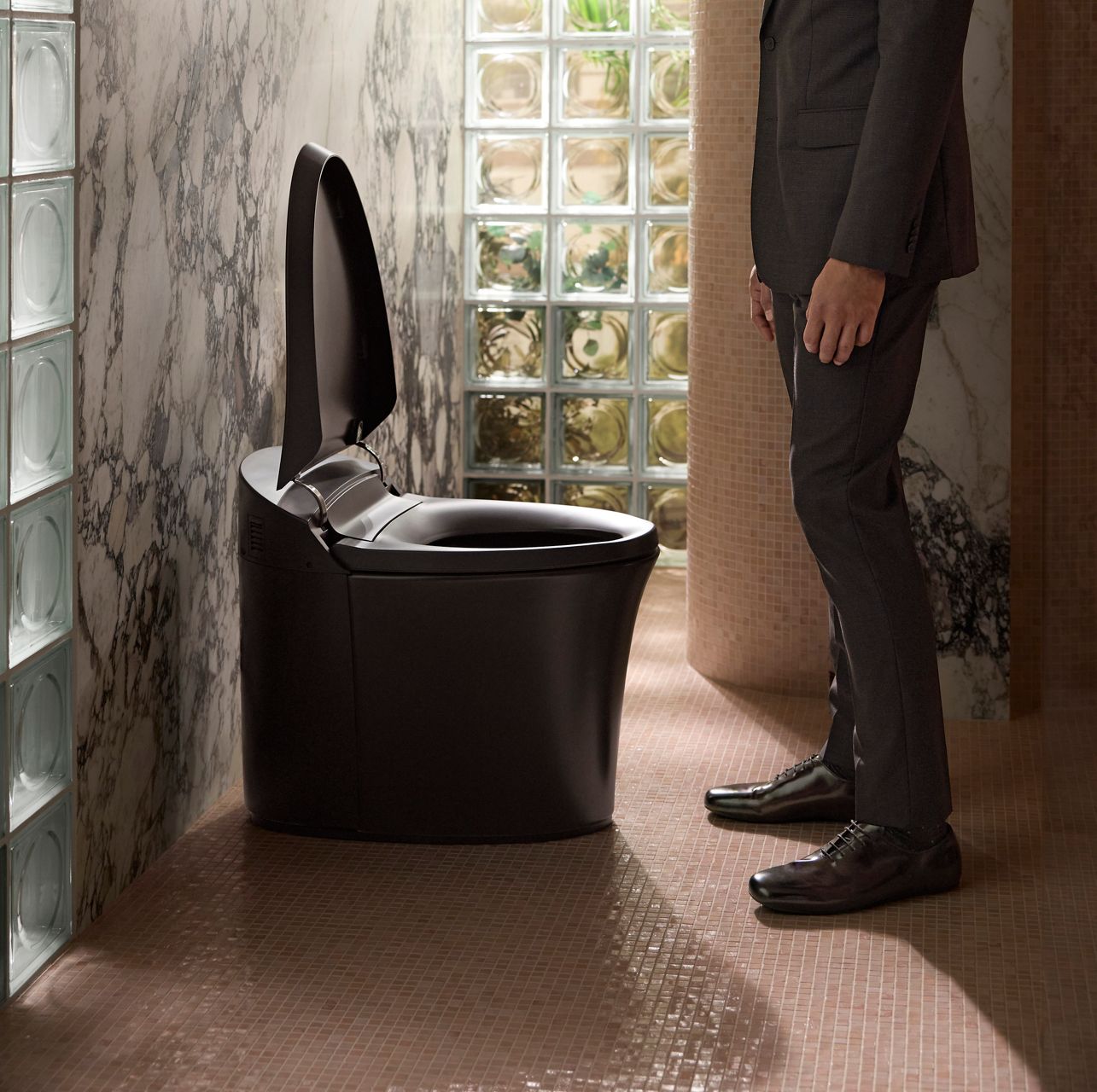 A person stands beside a sleek and modern black smart toilet with the lid open.