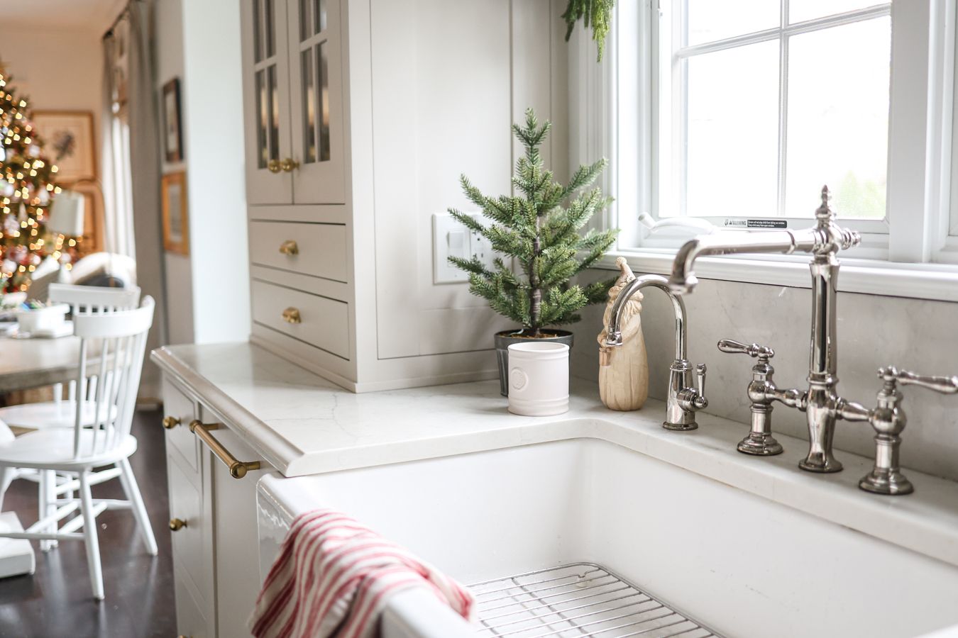 Alaina Kaz’s kitchen featuring polished chrome bridge faucet and farmhouse sink with mini evergreen holiday décor.