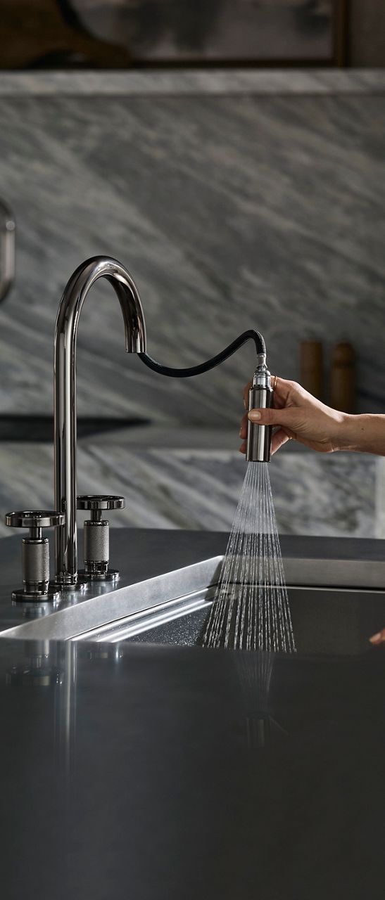 Pull-down kitchen faucet with spray head dispensing water into a stainless steel sink.