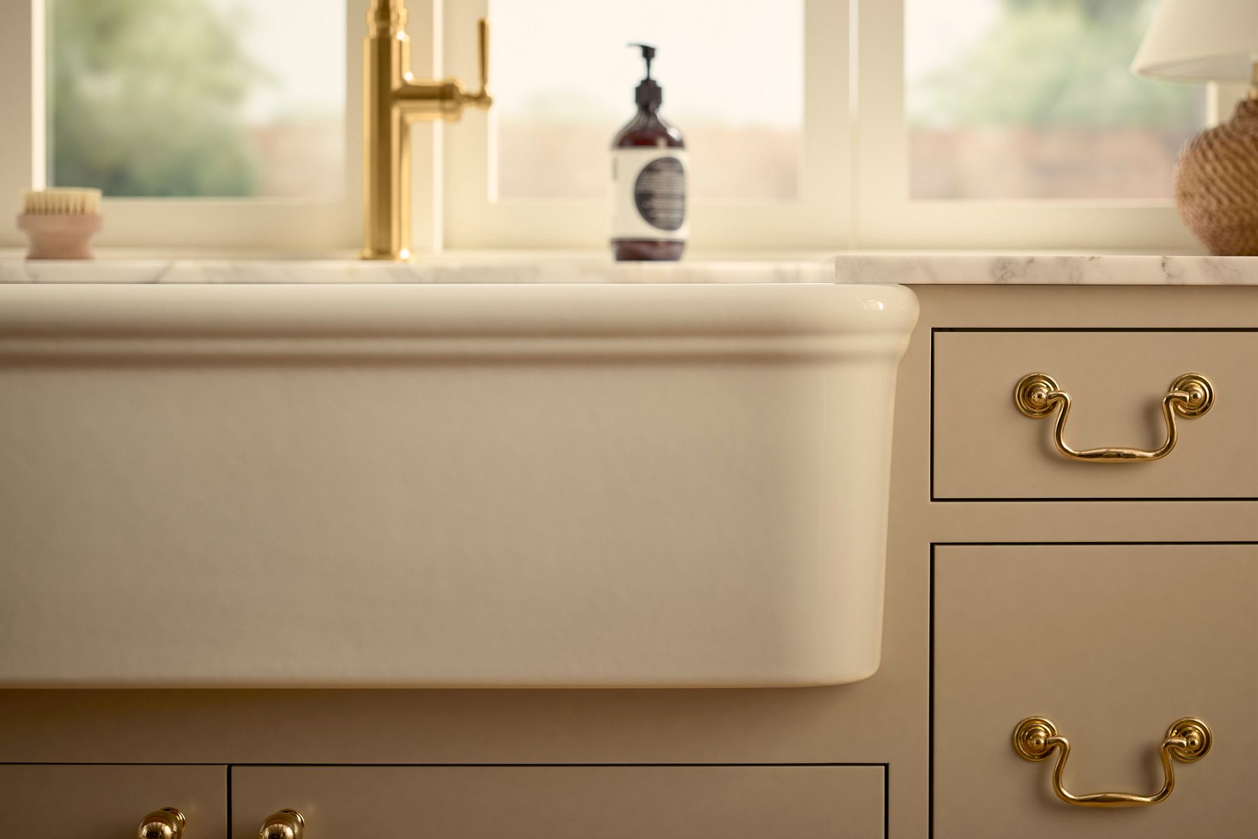 Bright kitchen with neutral cabinets, gold hardware, and an apron‑front sink.