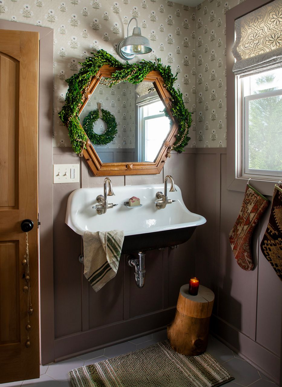 Jenni Yolo’s bathroom featuring hexagonal wood-framed mirror, wall-mounted faucets, and green holiday wreath.