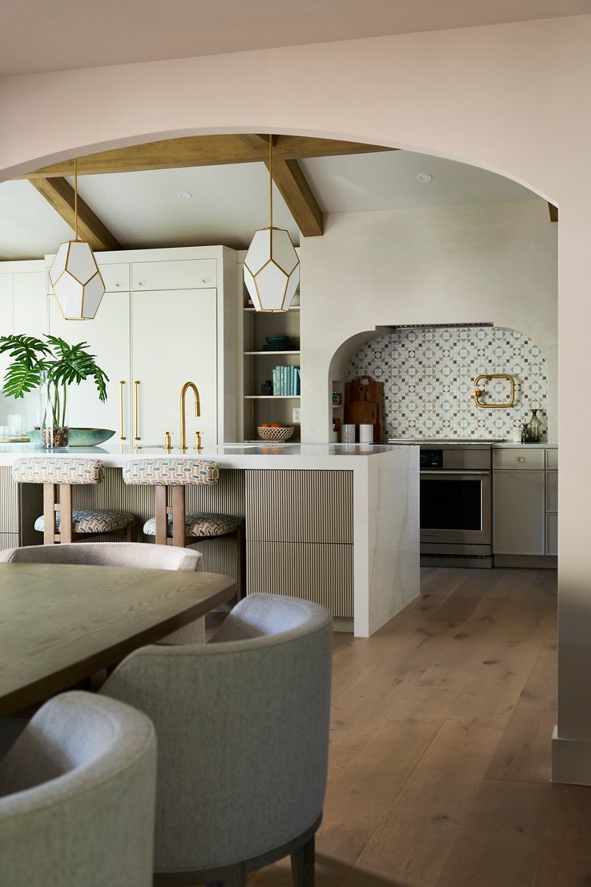 Open-concept kitchen featuring an island, brass fixtures, arched doorway, and warm neutral finishes.