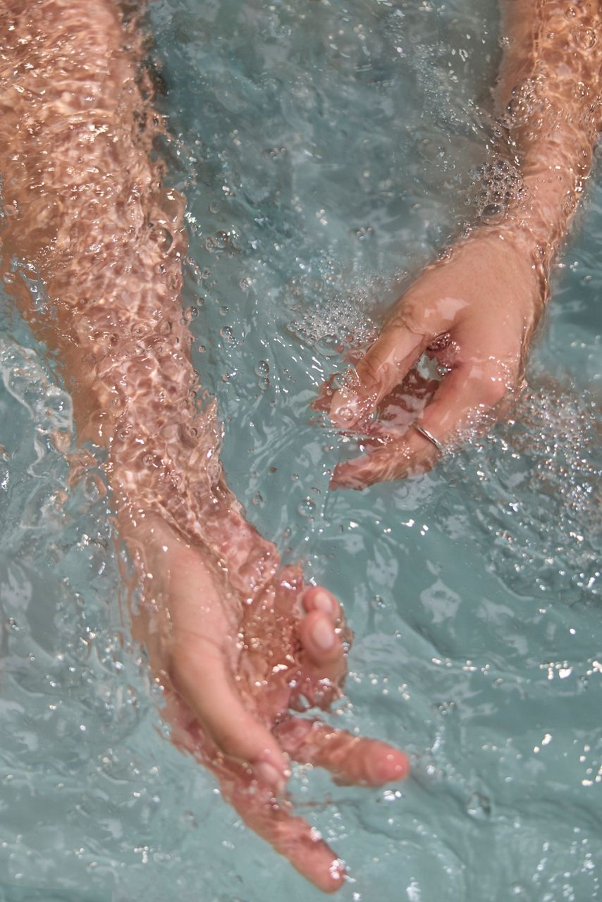 Close-up of hands submerged in gently rippling bath water, highlighting a relaxing soaking experience.