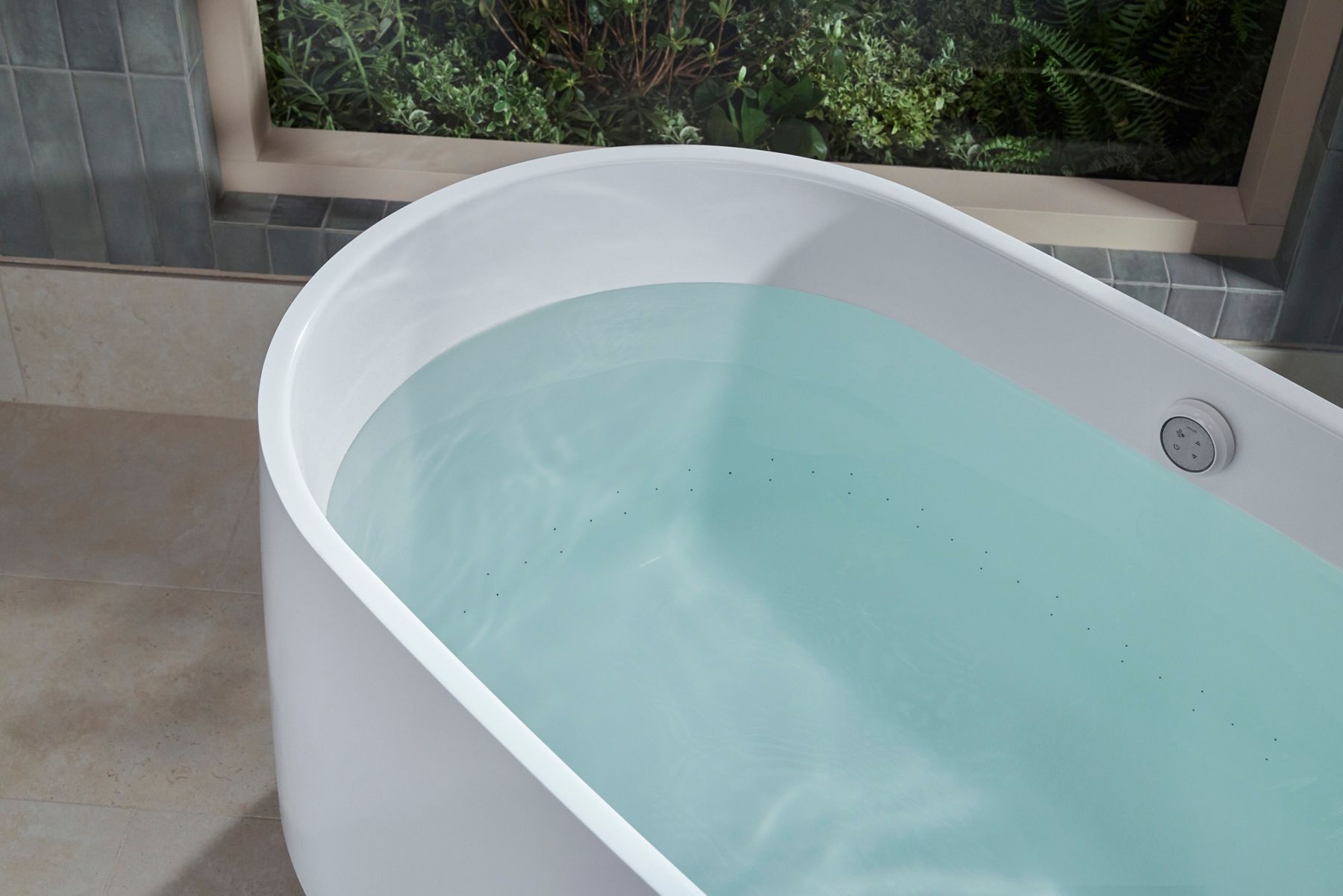 Close-up of a white freestanding bathtub filled with clear water, highlighting the integrated overflow drain and smooth contemporary design.