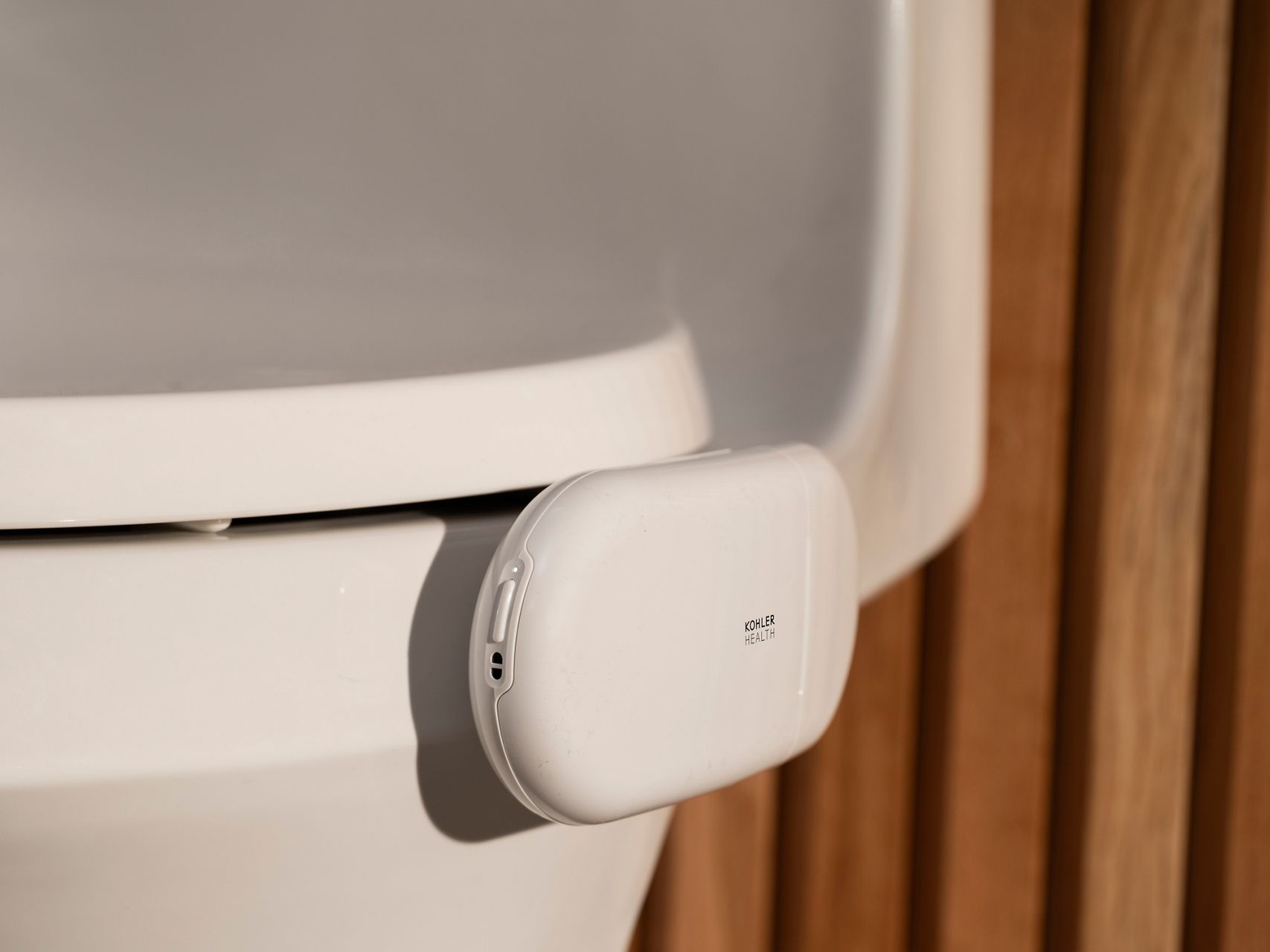 Close-up of the Kohler Health Dekoda device securely attached to the rim of a toilet using its adjustable clamp for tool-free installation.