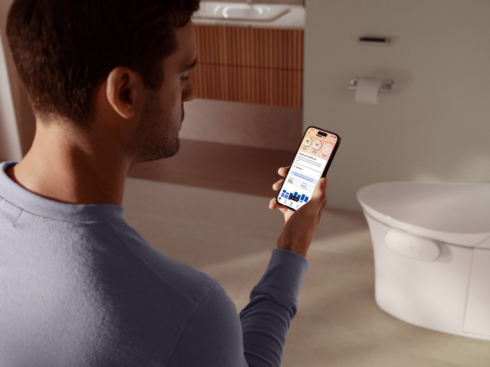 Person holding a smartphone displaying the Kohler Health app with personalized hydration and gut health insights collected by the Dekoda device.