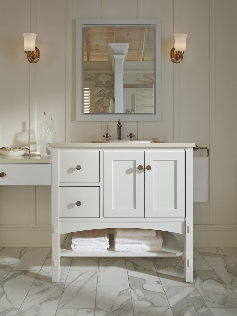 A white marbou vanity with a cream-colored top, brushed bronze hardware and a brushed bronze Artifacts faucet in a bathroom with cream colored walls.