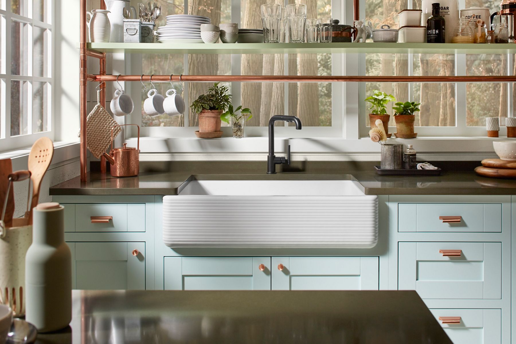 Front view of a Whitehaven Hayridge farmhouse undermount sink in a light blue cabinet with a brown stone counter top and matte black kitchen faucet.