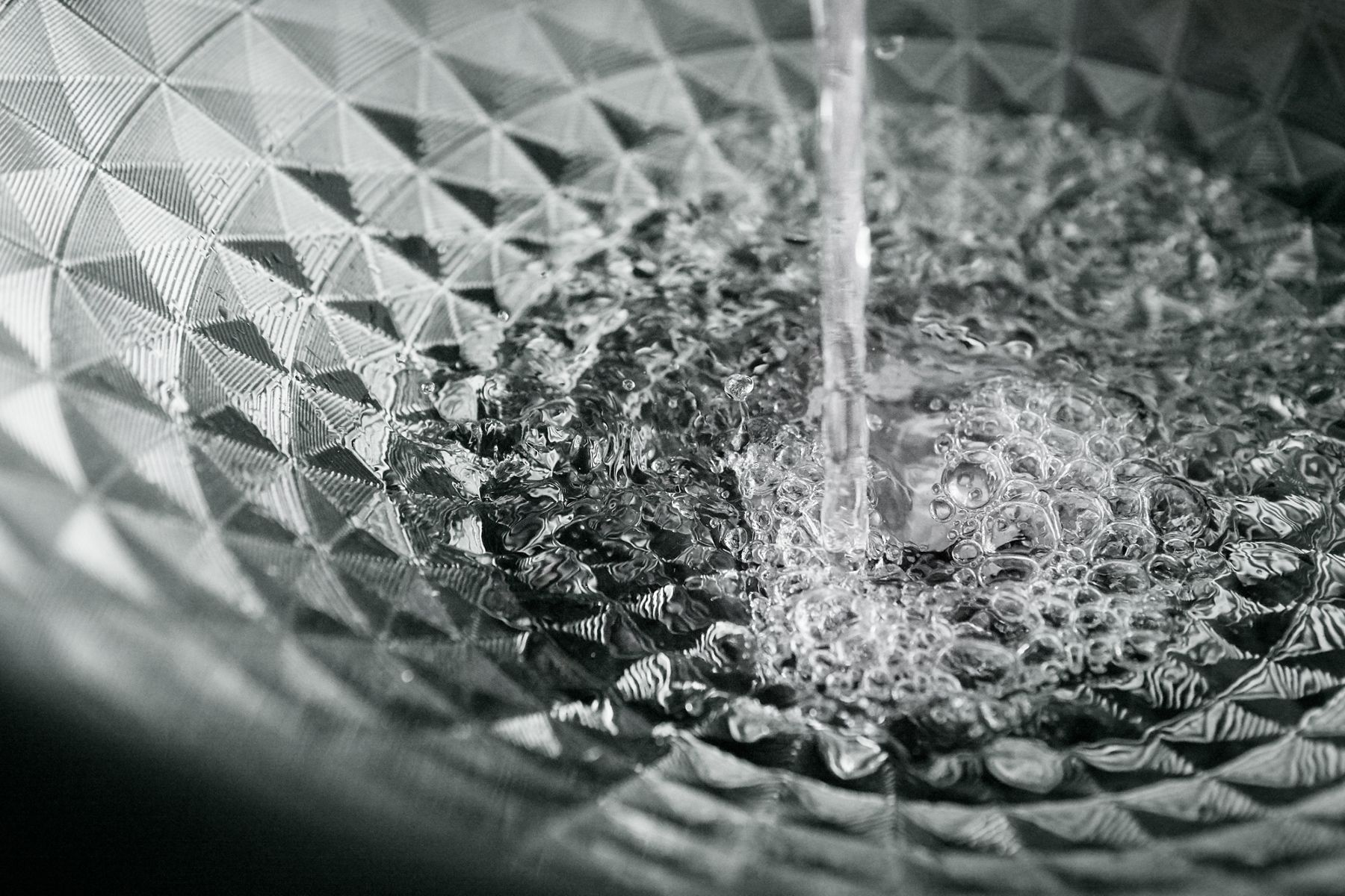 Water pouring into a glass bathroom sink with square shapes in a circular pattern around its circumference.