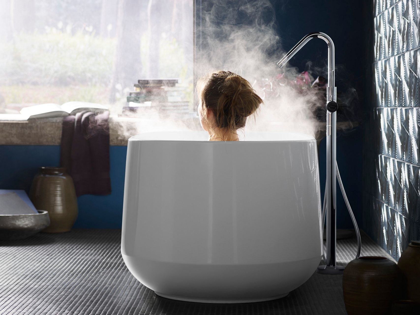 La tête d’une femme se lève au-dessus d’une baignoire autoportante KOHLER alors qu’elle s’y baigne.