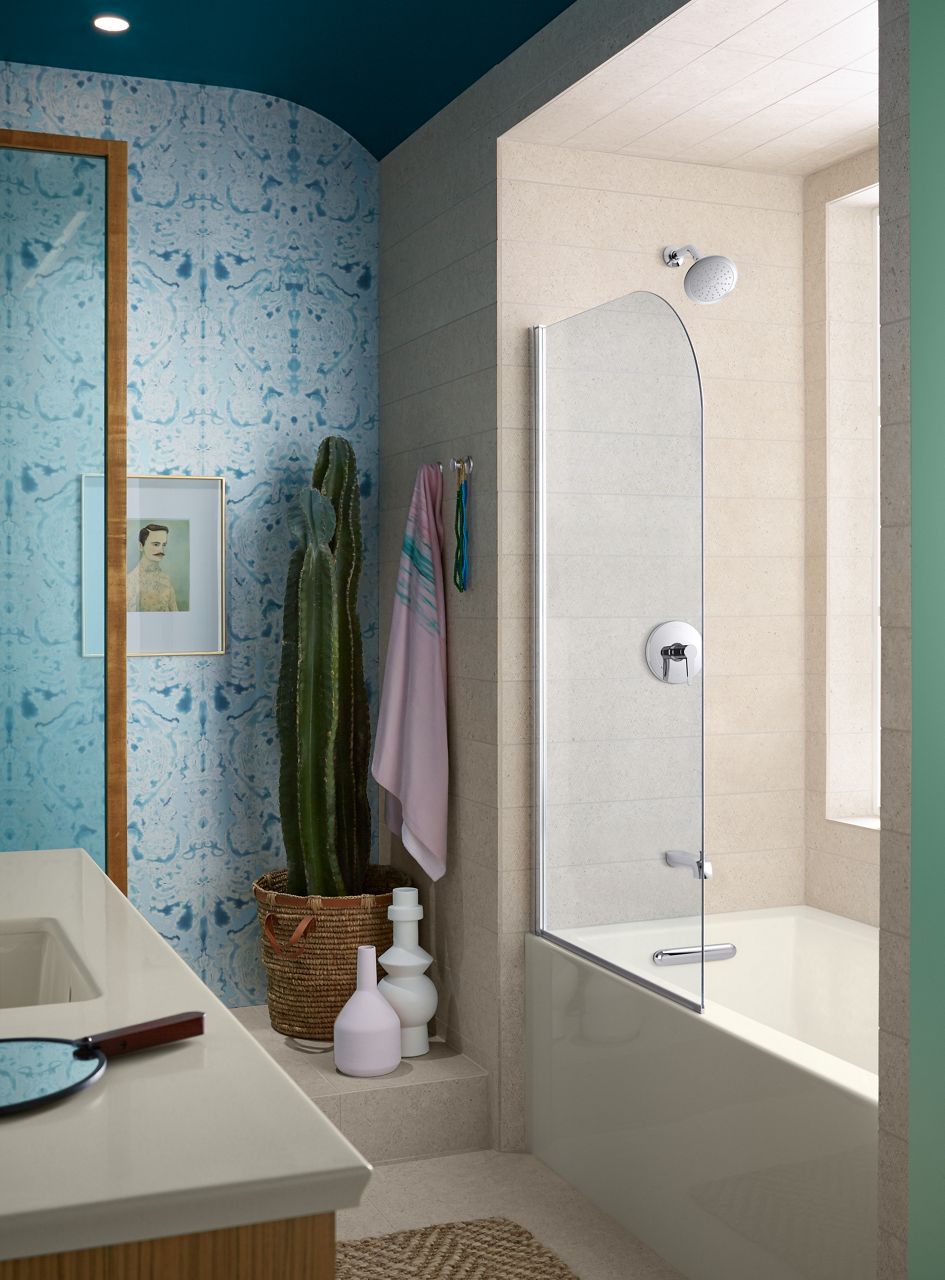 KOHLER bath screen with white alcove tub with beige walls in a bathroom with light blue accent wall and a cactus in the corner.