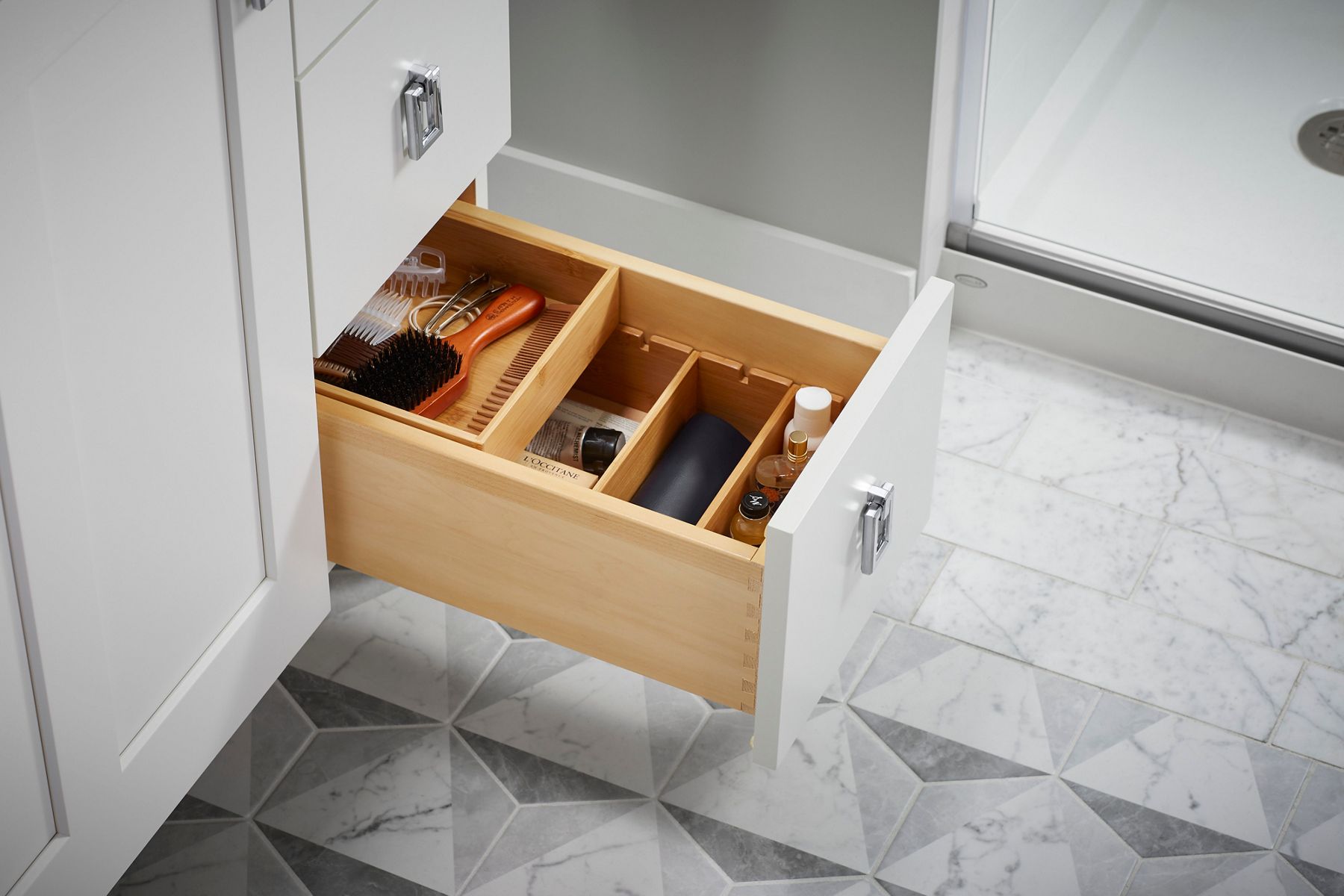A white vanity with a drawer pulled open to show a variety of tiered containers holding a range of bathroom products.