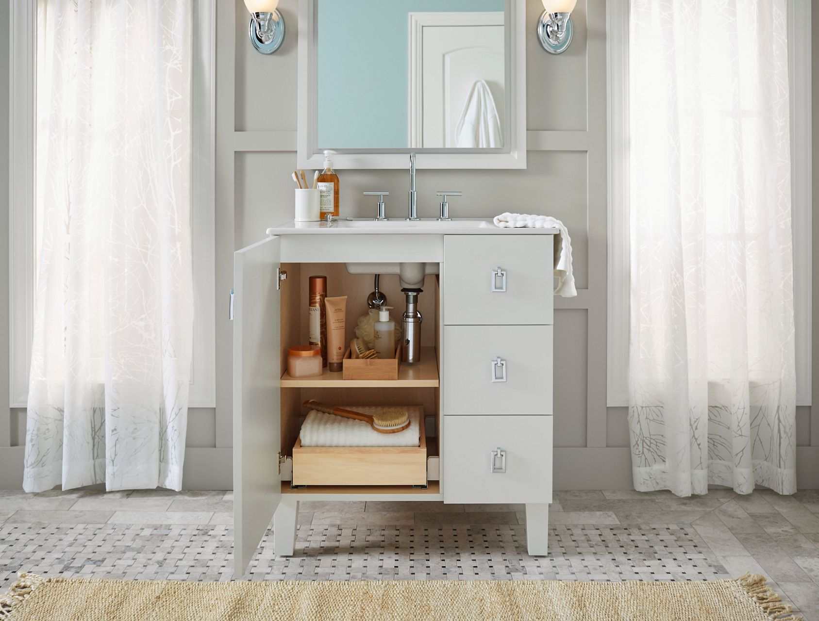 A white vanity with the left door open to reveal a pull-out drawer on the bottom and a shelf in the middle with a range of bathroom products on it.