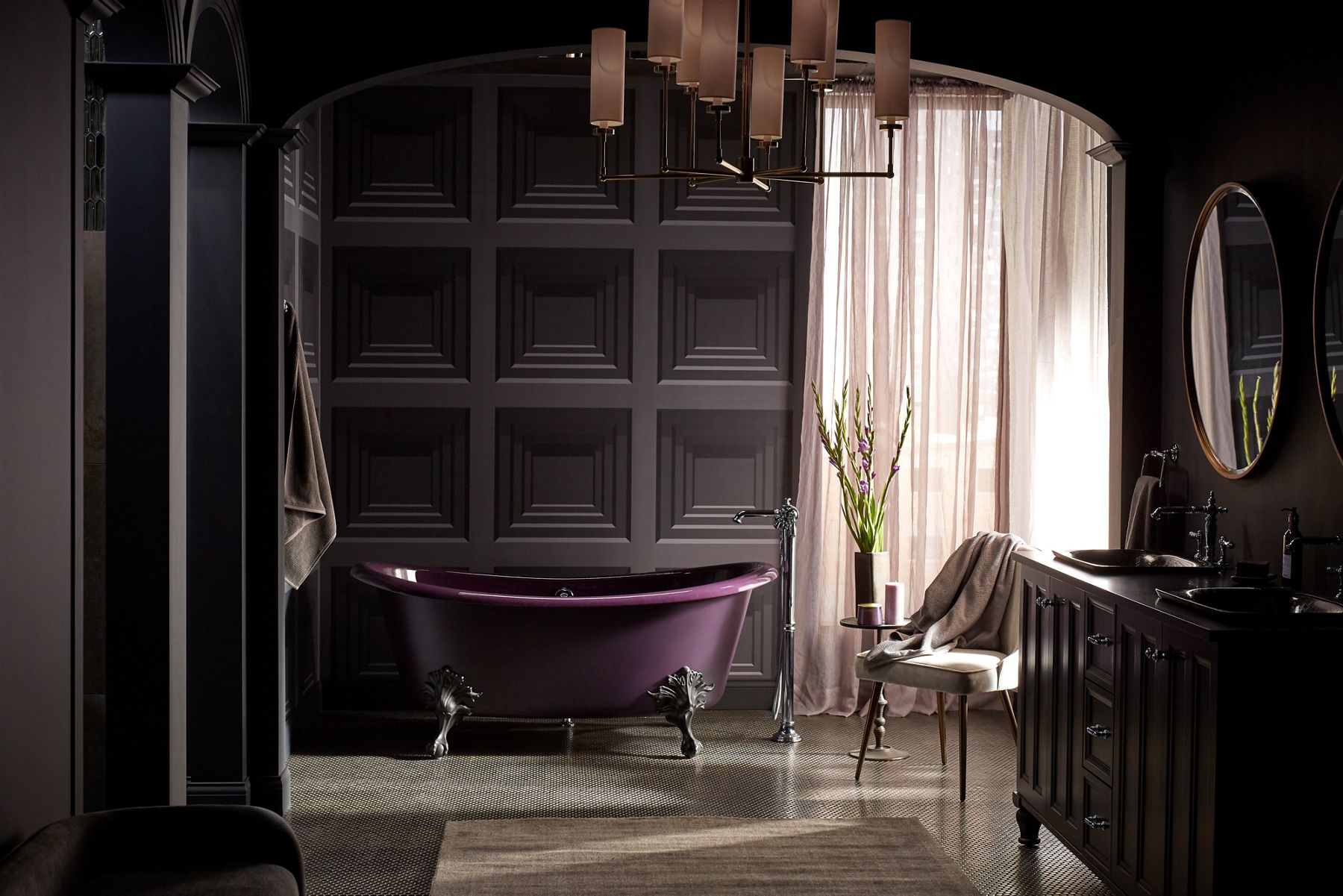 A dark plum freestanding bath with black claw feet in front of a dark gray square paneled wall.