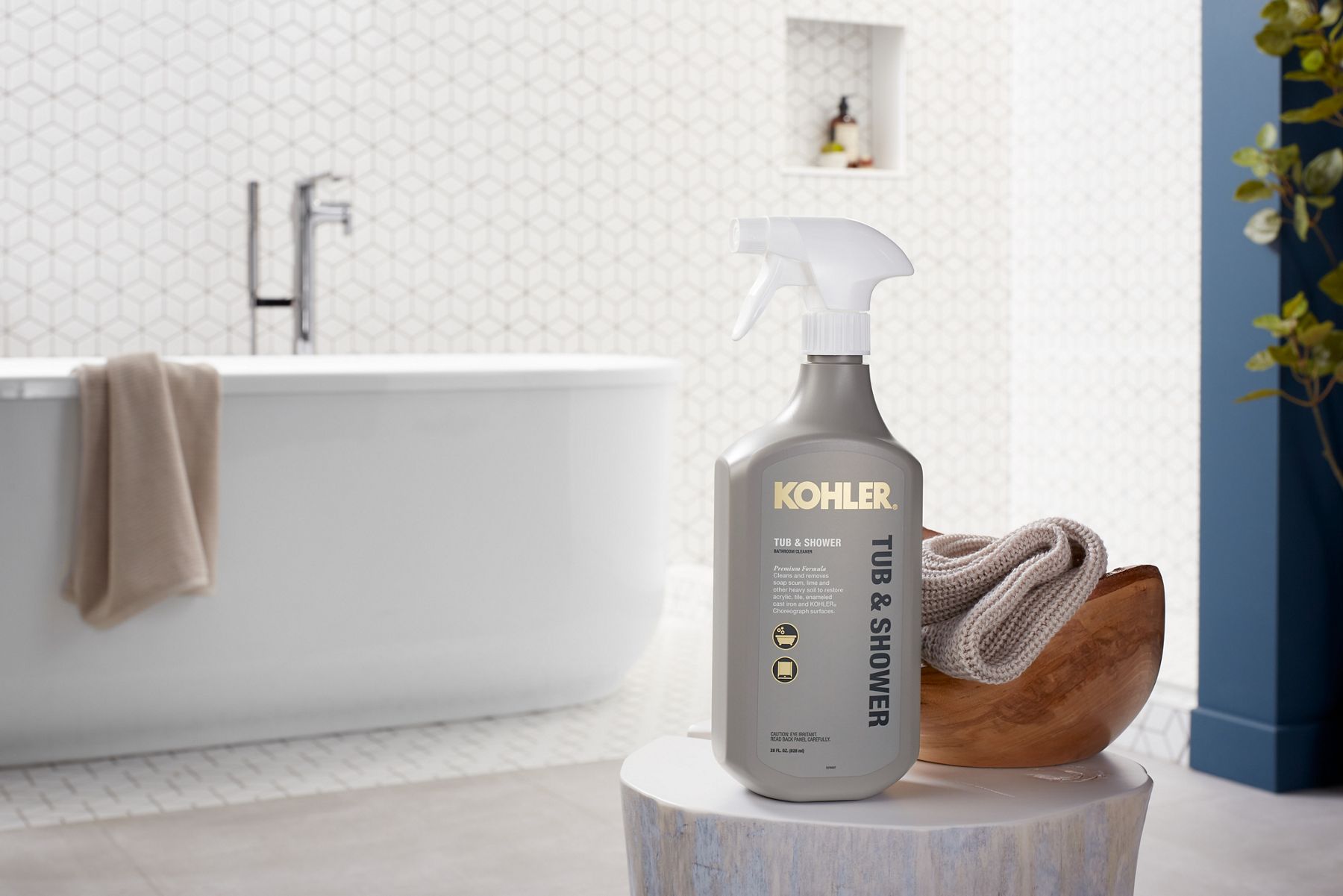 A spray bottle of KOHLER tub and shower cleaner with washcloth in a bathroom with freestanding tub.