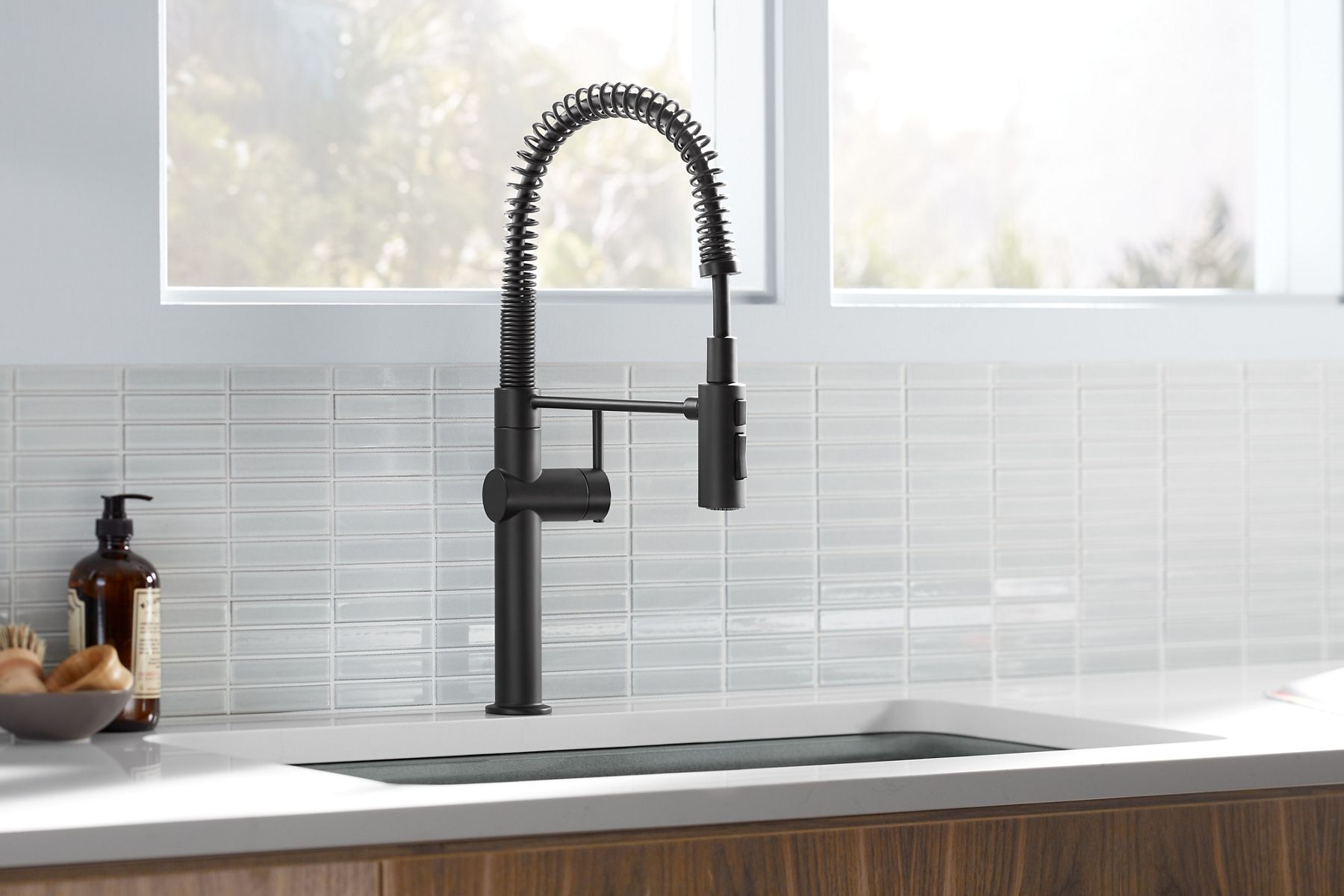 A matte black Kohler pull-out kitchen faucet adds contrast to a white counters and a white tile backsplash.