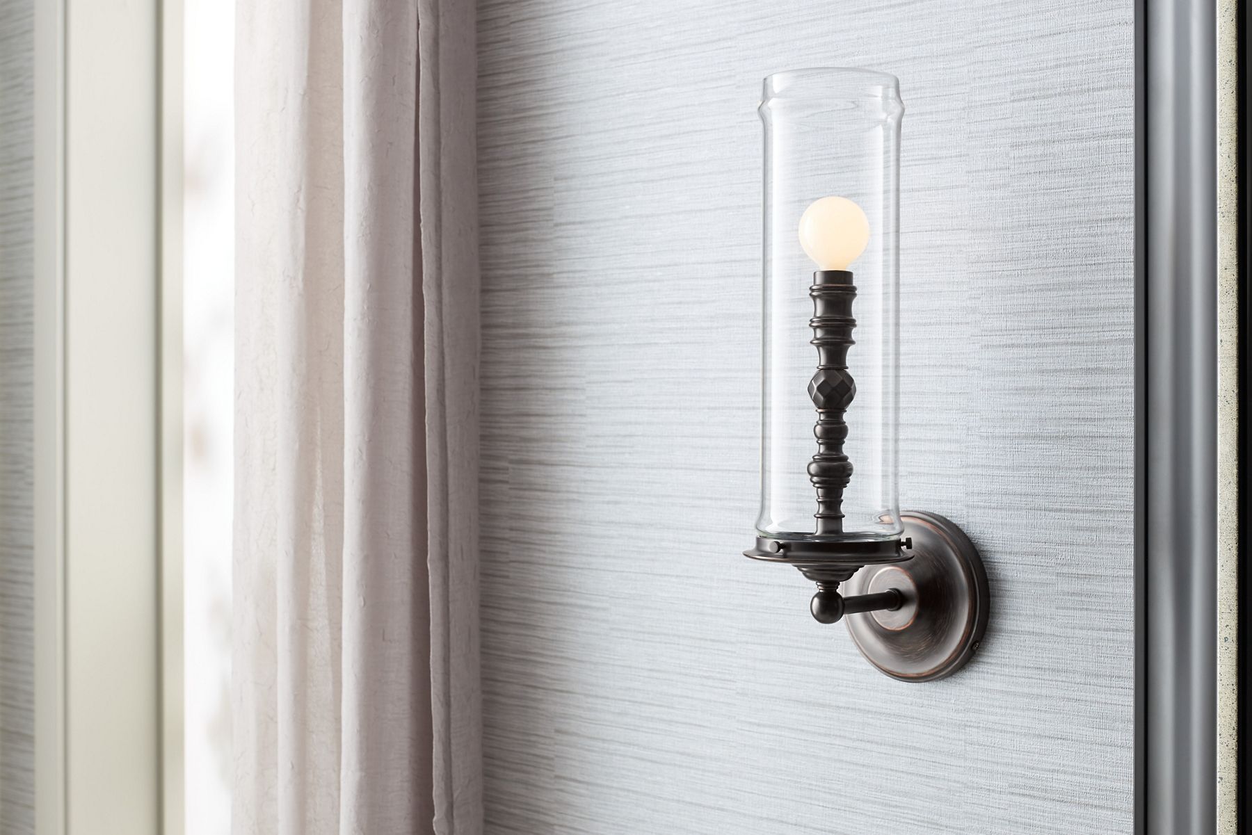 Close up of a sconce light with ornate detailing and a large glass tube enclosing the stem of the light.