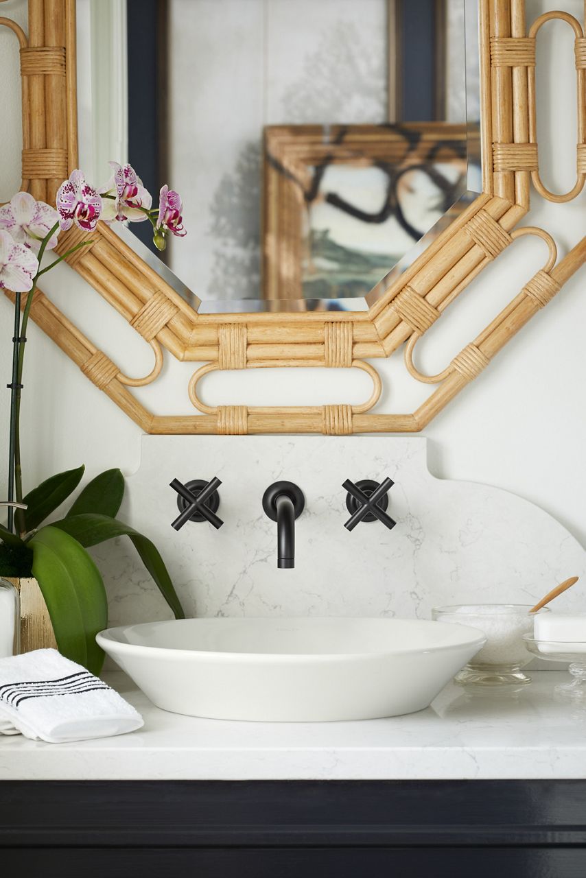 Wall-mounted bathroom faucet with black cross handles over a vessel sink.