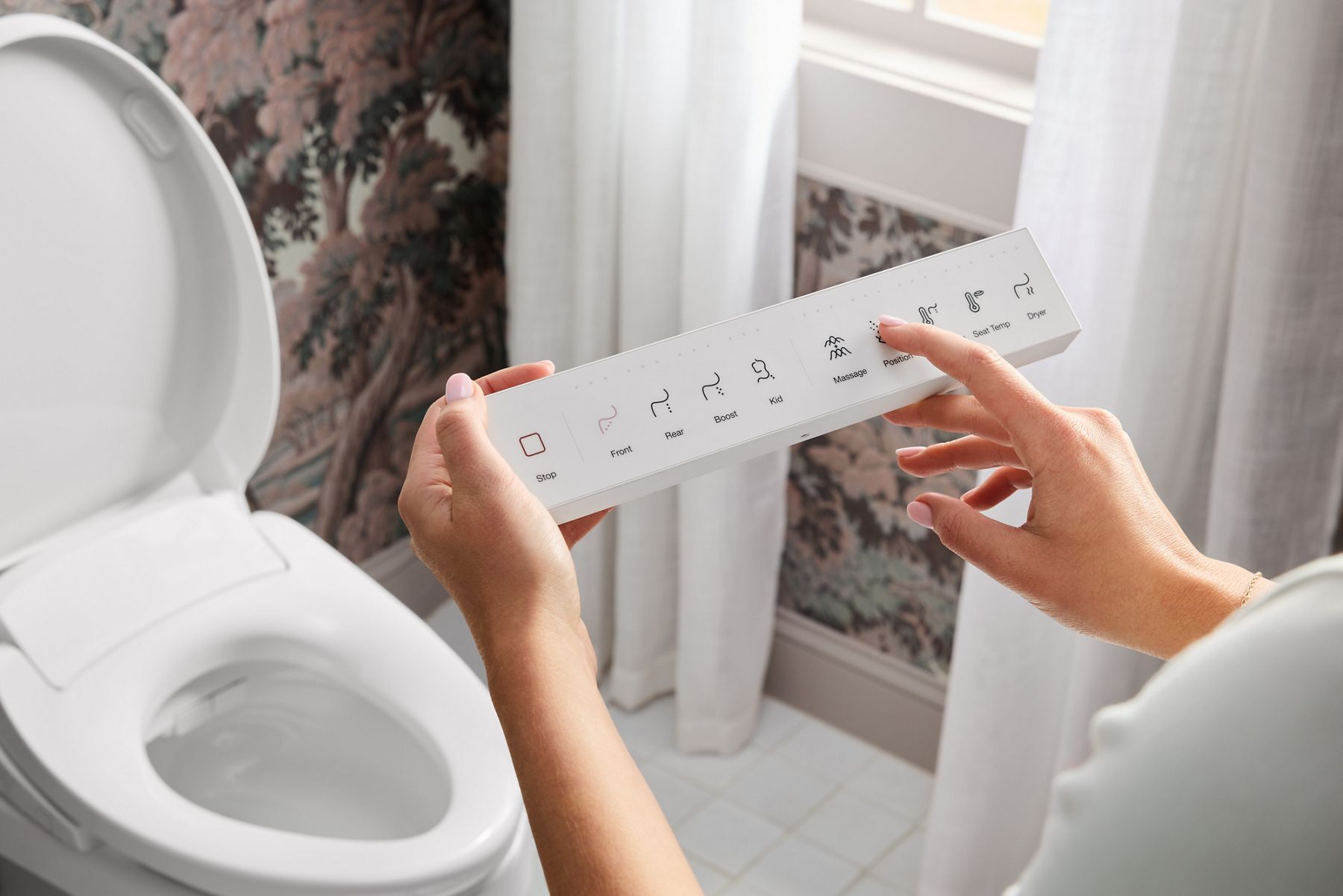 Hands holding a bidet seat remote control next to a toilet with the lid open