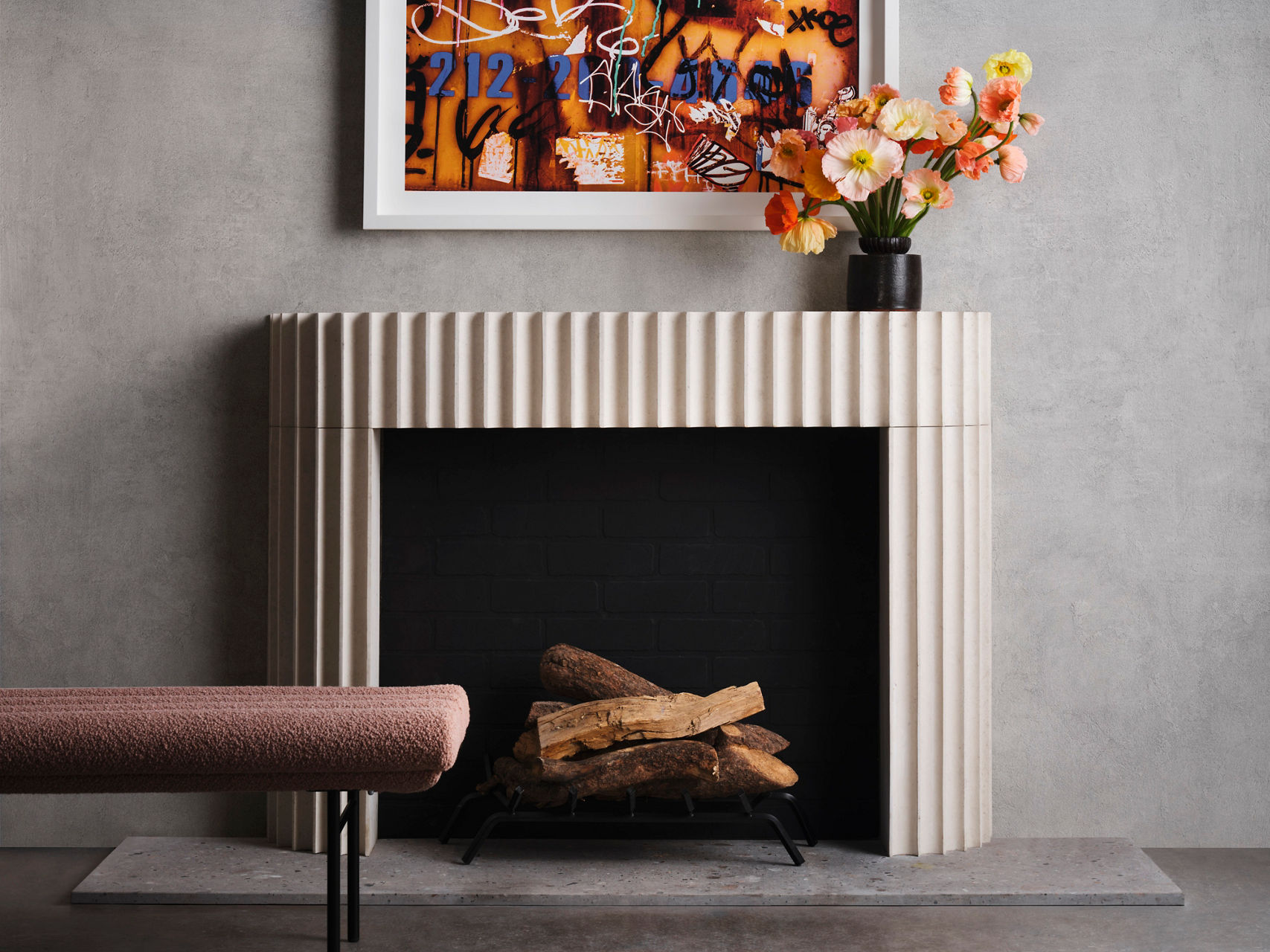 Modern stone fireplace with fluted surround, black firebox, and stacked wood, accented by contemporary artwork and floral decor.
