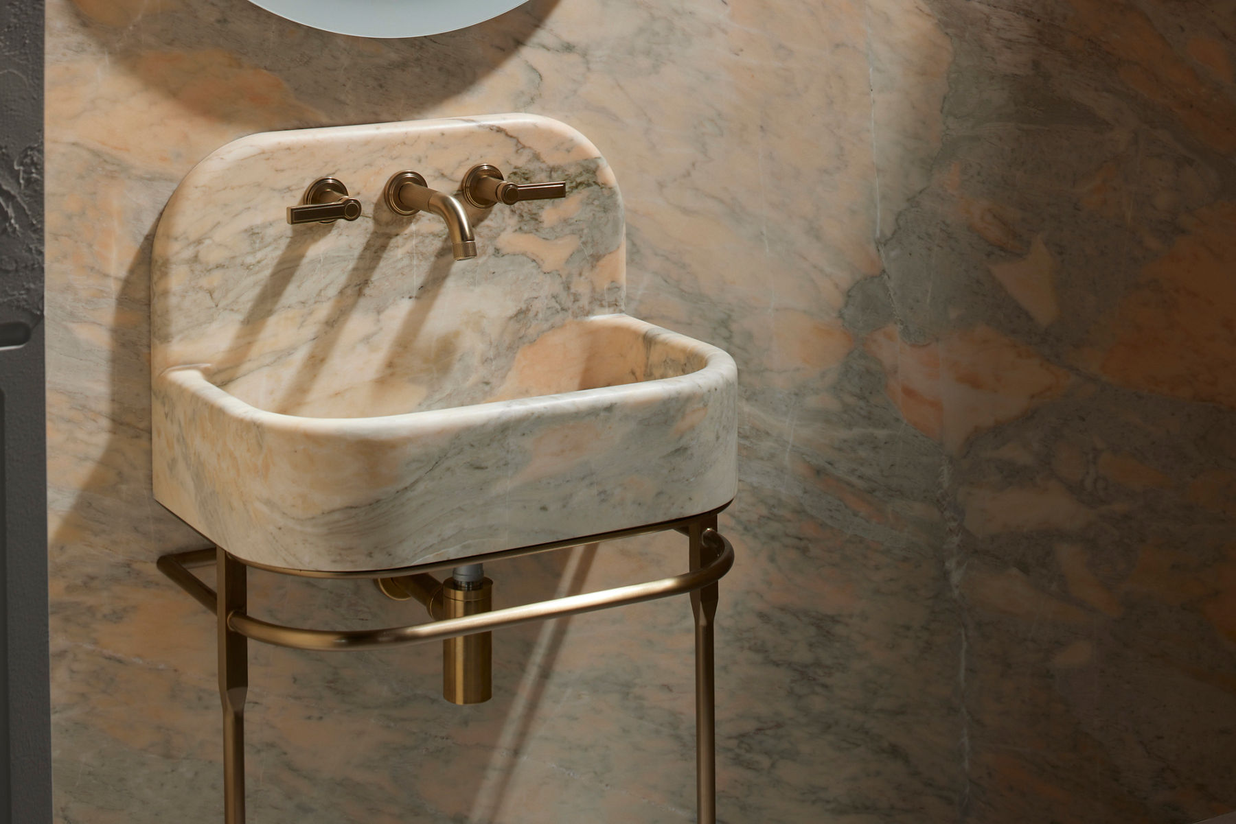 Luxury stone vanity sink with integrated backsplash and wall-mounted brass faucet in a marble bathroom setting