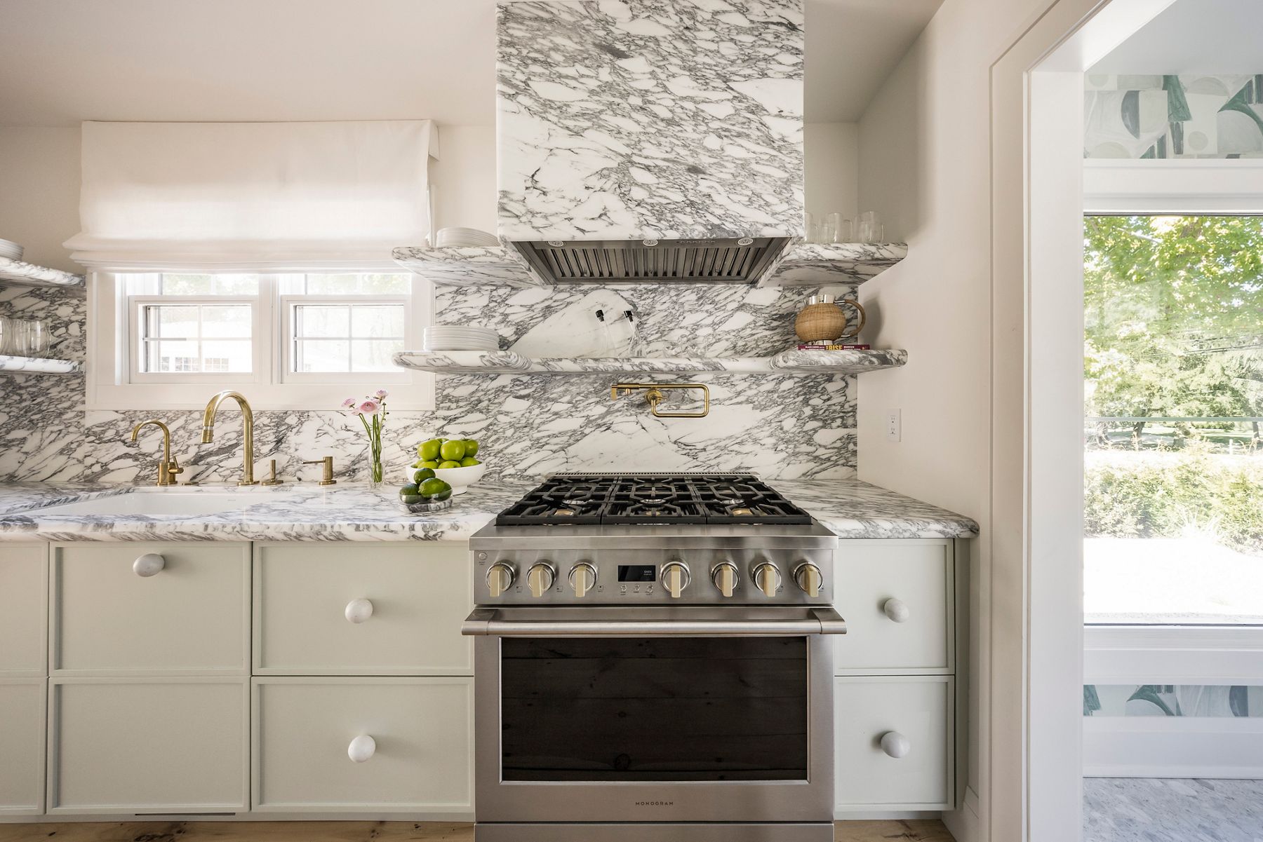 Marble slab backsplash with full-height veined stone in luxury white kitchen, continuous countertop and floating shelves, showcasing seamless slab backsplash design behind professional range and brass fixtures