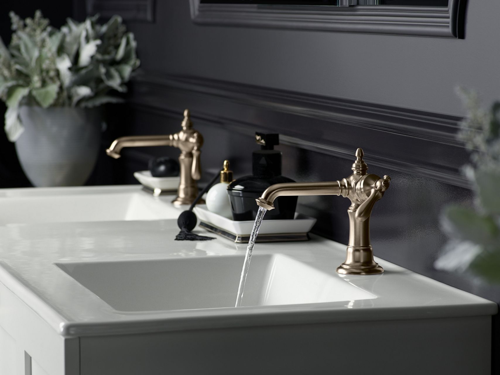 Side view of vintage inspired brushed bronze bath sink faucets on a white countertop against black walls