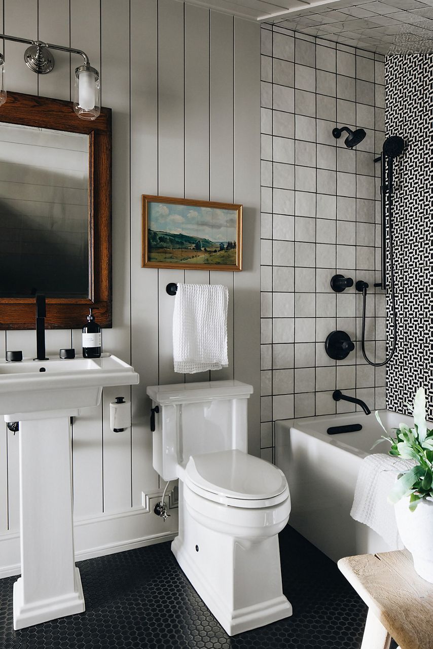 A bathroom with white KOHLER Tresham pedestal sink, white Tresham toilet, and tub shower with contrasting black and white tile.