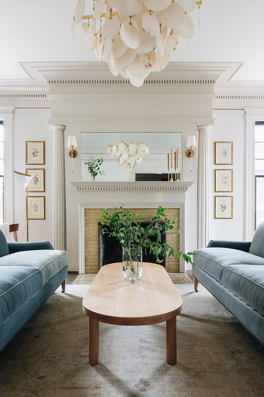 Des colonnes cannelées blanches encadrent une cheminée avec manteau et garniture blancs, et un grand miroir reflétant un grand lustre, dans un salon avec des canapés en velours bleu clair.