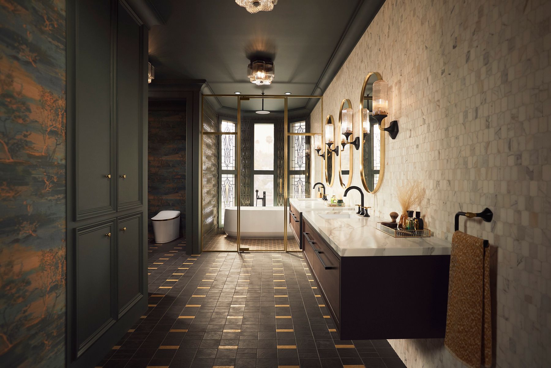 Les carreaux blancs, les accents noirs et dorés et le marbre clair ajoutent une touche de glamour à une salle de bain avec des meubles-lavabos à montage mural, une baignoire autoportante blanche Ceric de KOHLER positionnée dans une baie de fenêtre et une toilette monopièce Eir blanche dans une alcôve séparée.