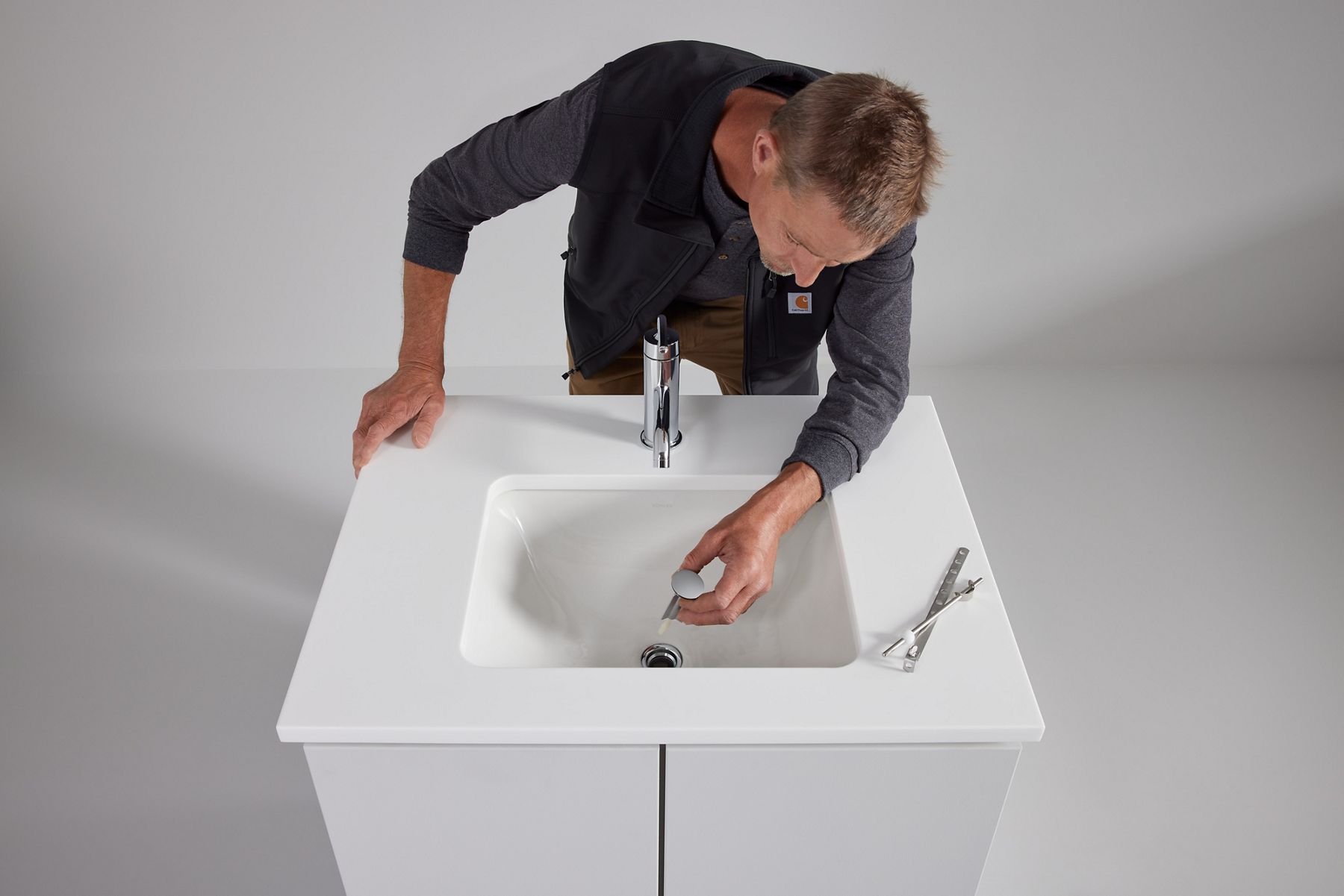 A man leaning over a sink and faucet, installing the drain plug.