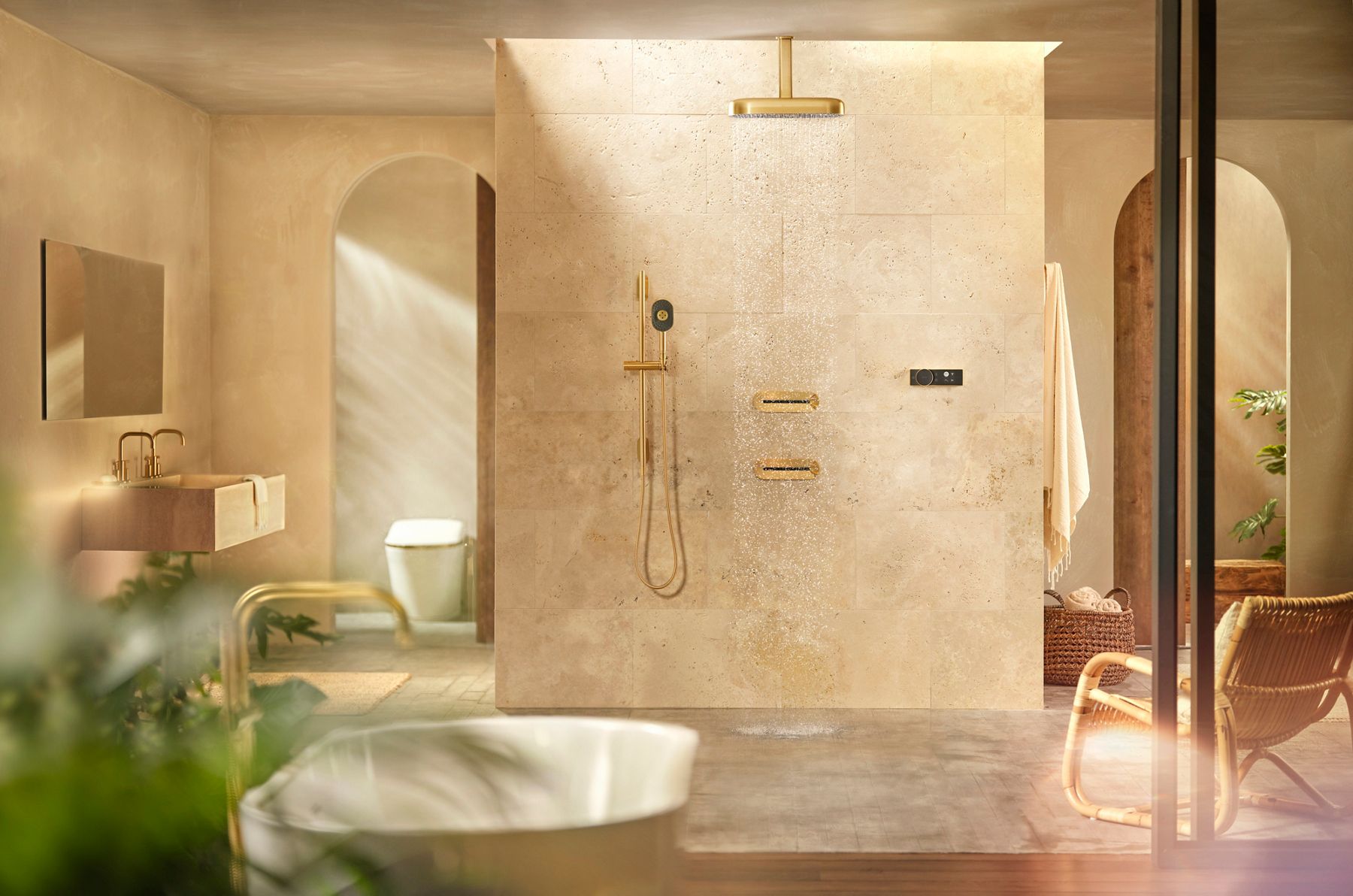 Un assortiment de composants de douche Statement en laiton brossé moderne dans une grande zone de douche ouverte avec des murs et des planchers en pierre de couleur crème.